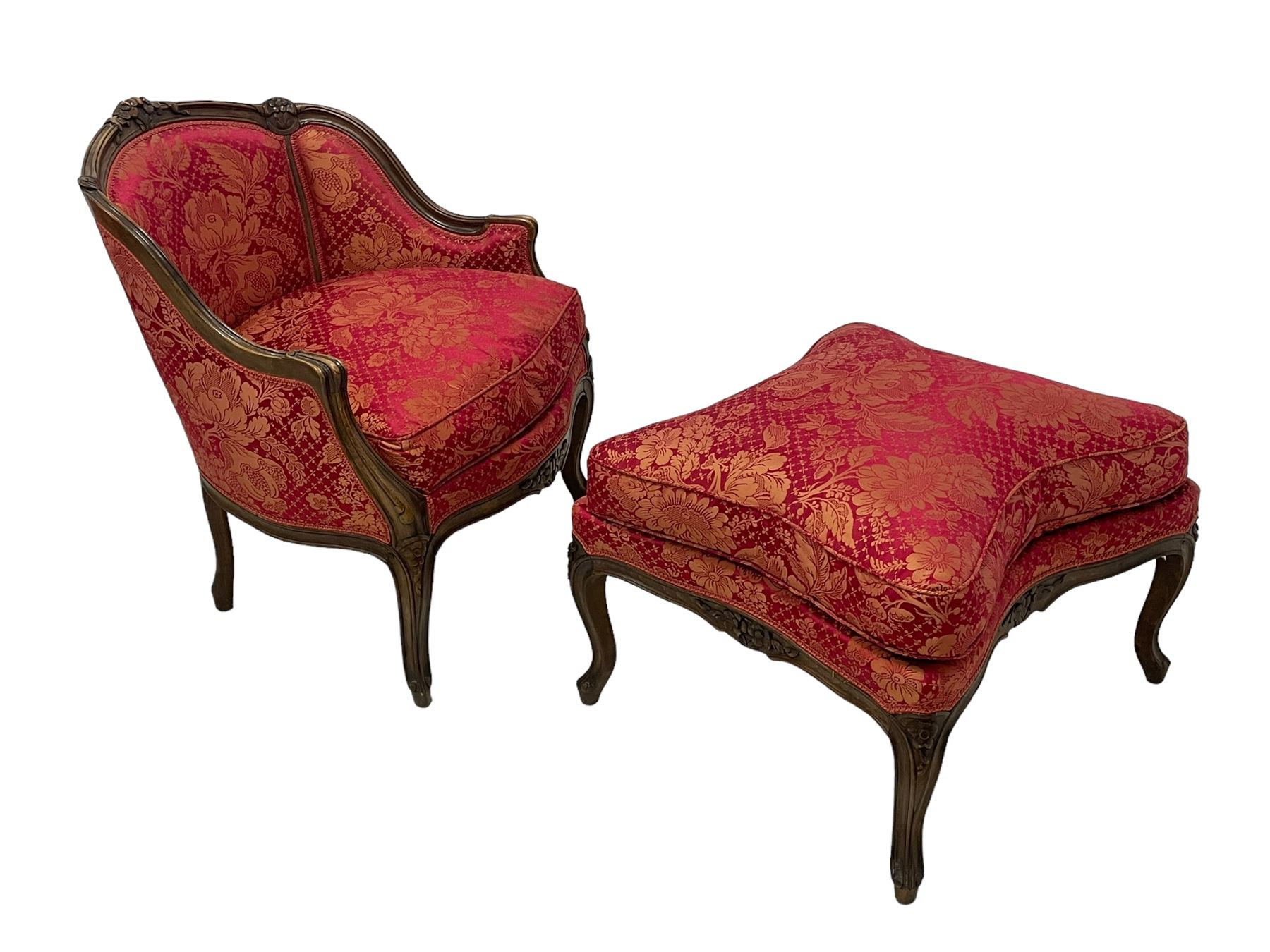 Late 20th century French design stained beech framed armchair and matching stool - the armchair with shaped and moulded frame carved with flower heads and foliage, upholstered in silk red and gold ground fabric with floral pattern, on scroll carved cabriole feet decorated with flower head carvings (W73cm, H82cm, D75cm); the footstool of concaved rectangular form with moulded frame carved with flower heads, upholstered loose cushion, on cabriole feet (70cm x 64cm, H48cm)