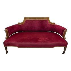 Late Victorian inlaid walnut two seat settee, the shaped cresting rail decorated with foliate inlays and boxwood stringing, upholstered in crimson velvet with sprung seat, raised on turned and fluted supports with ceramic castors