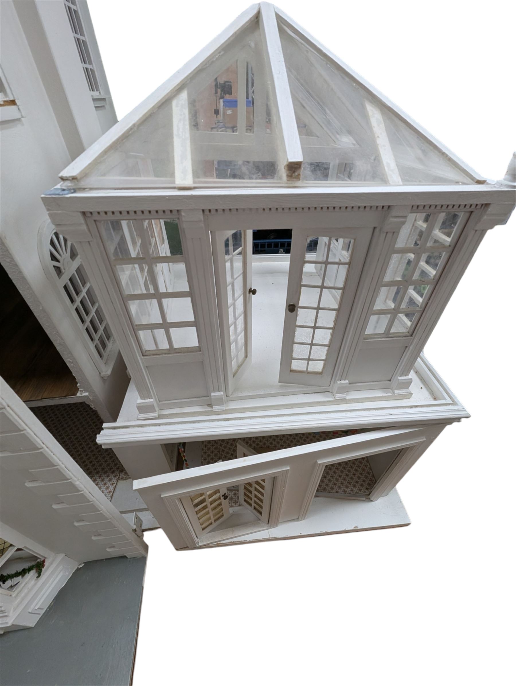 Large three storey modern dolls house, painted white with latticed windows, grey roof and metal fencing, with decorated interior, together with two dolls house garden rooms and two conservatories