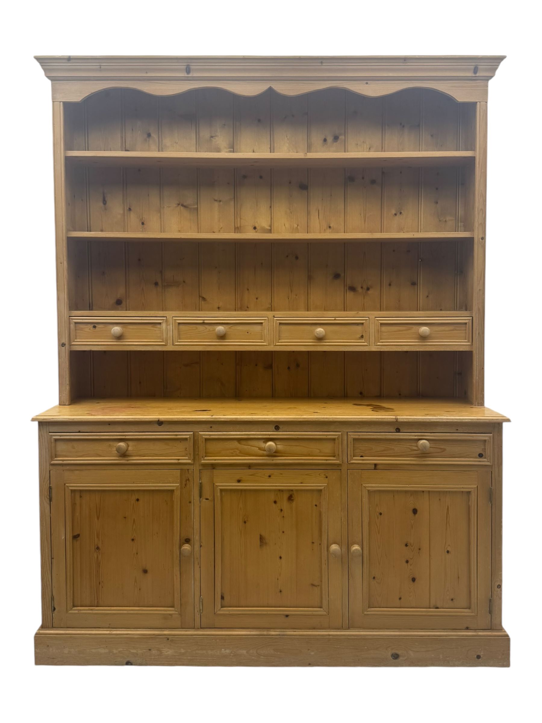 Traditional design waxed pine dresser, upper section with moulded cornice over scalloped frieze, fitted with two open shelves and four drawers, lower section with three drawers over three panelled cupboards, on plinth base