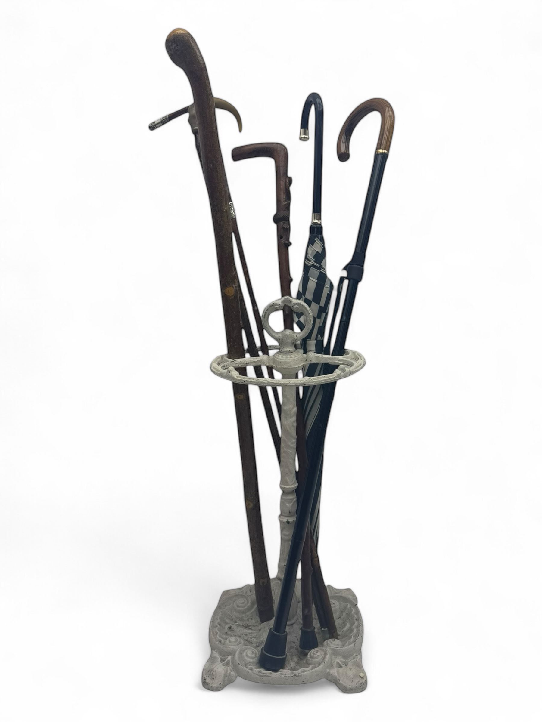 Victorian design cast iron umbrella stand, ornate stem on shell C-scroll base; together with a collection of walking sticks including a silver tipped cane 