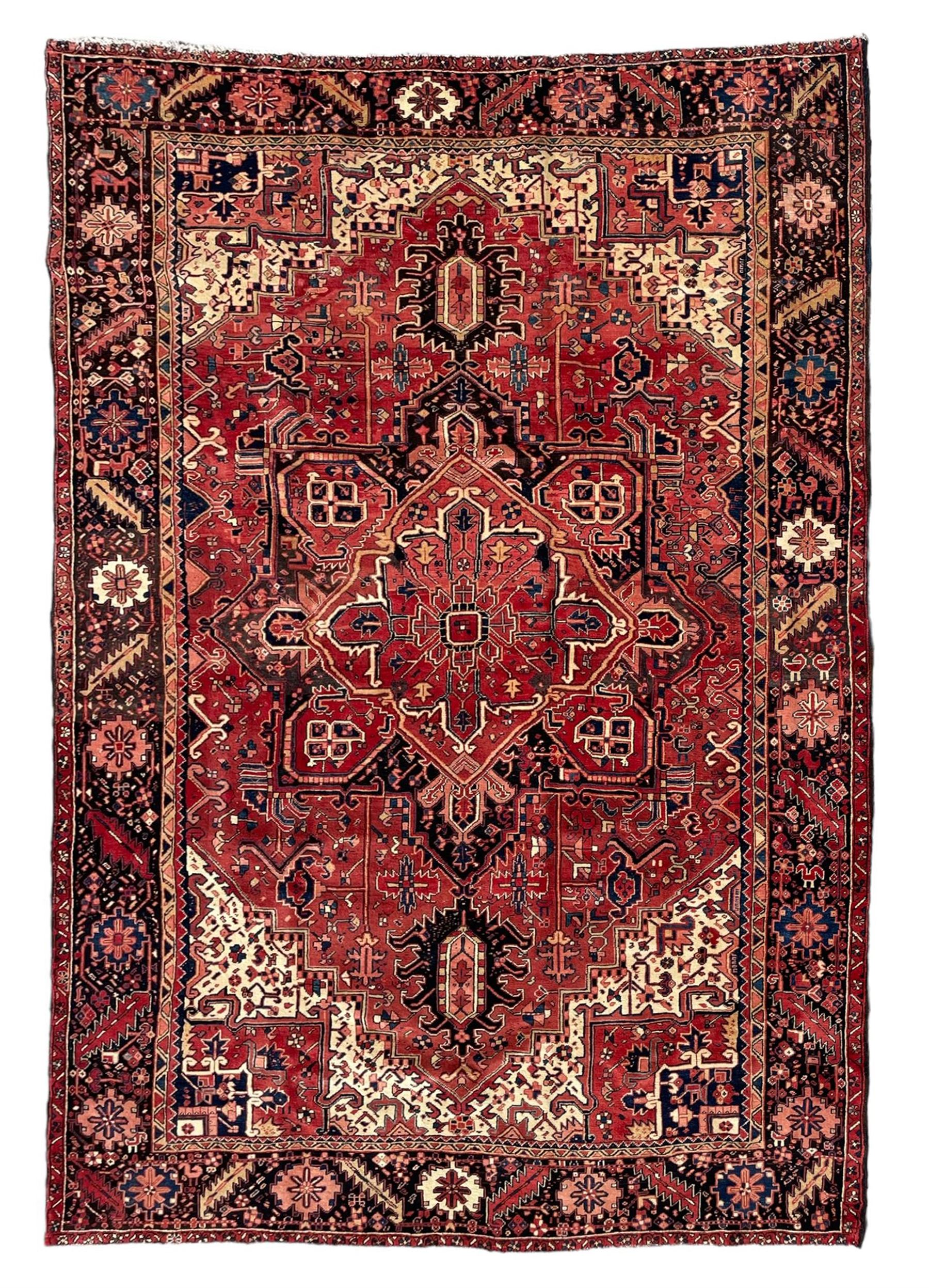 Persian Heriz red ground carpet, large central eight point medallion with projecting palmettes surrounded by small geometric motifs, decorated profusely with hooks, rosettes and animals, the busy border decorated with stylised foliate motifs within guard stripes 