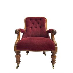 Victorian mahogany framed open armchair, upholstered in buttoned red fabric, the arm terminals carved with scrolls, on turned front supports with brass cups and castors