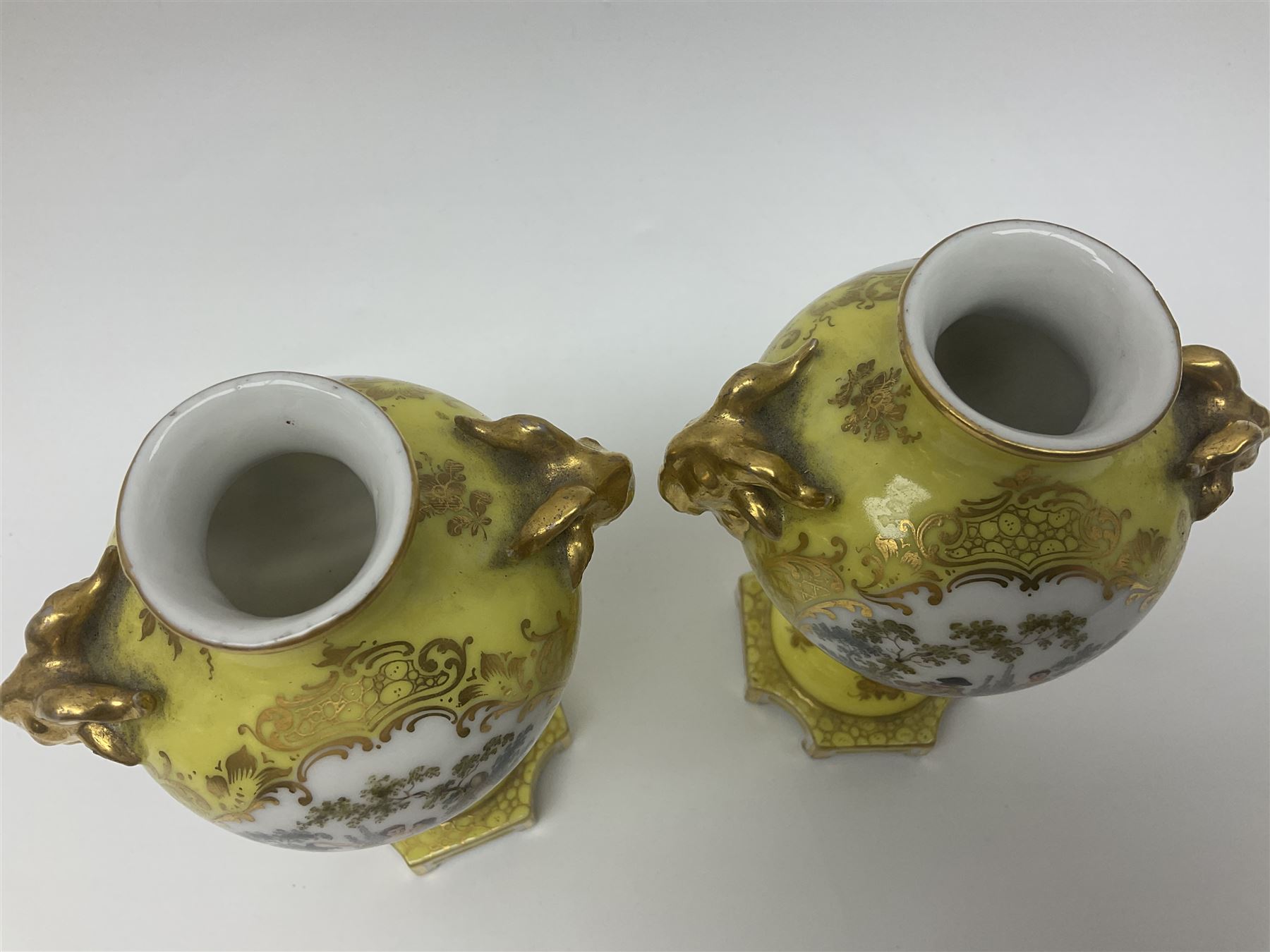 Pair of early 20th century Dresden vases with cover, of baluster form, decorated with figural panels within ornate gilt borders upon a yellow ground, with twin gilt goat mask handles, H16.5cm