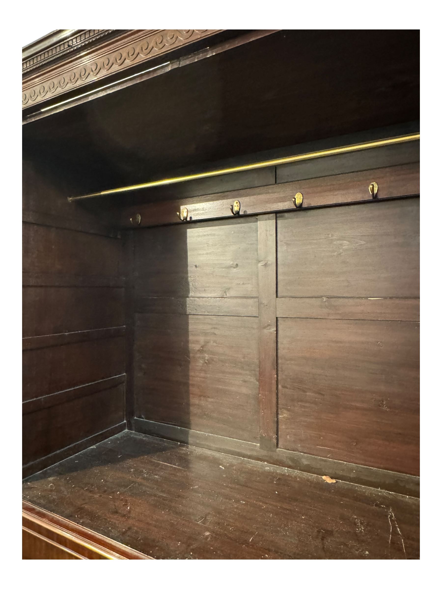 Victorian mahogany linen press, projecting cornice with dentil and scroll detailing, double panelled doors opening to an interior fitted with a brass hanging rail and coat hooks, lower section with two drawers and fitted shelves for additional storage, raised on bracket feet