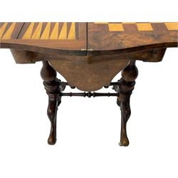 Victorian inlaid figured walnut games table, the serpentine fold-over top inlaid with scrolling foliate decoration, the top opens to reveal cribbage, backgammon and chess boards, single drawer over sliding storage well, on twin pillar supports united by double turned stretchers, on foliage carved out-splayed supports with brass and ceramic castors 