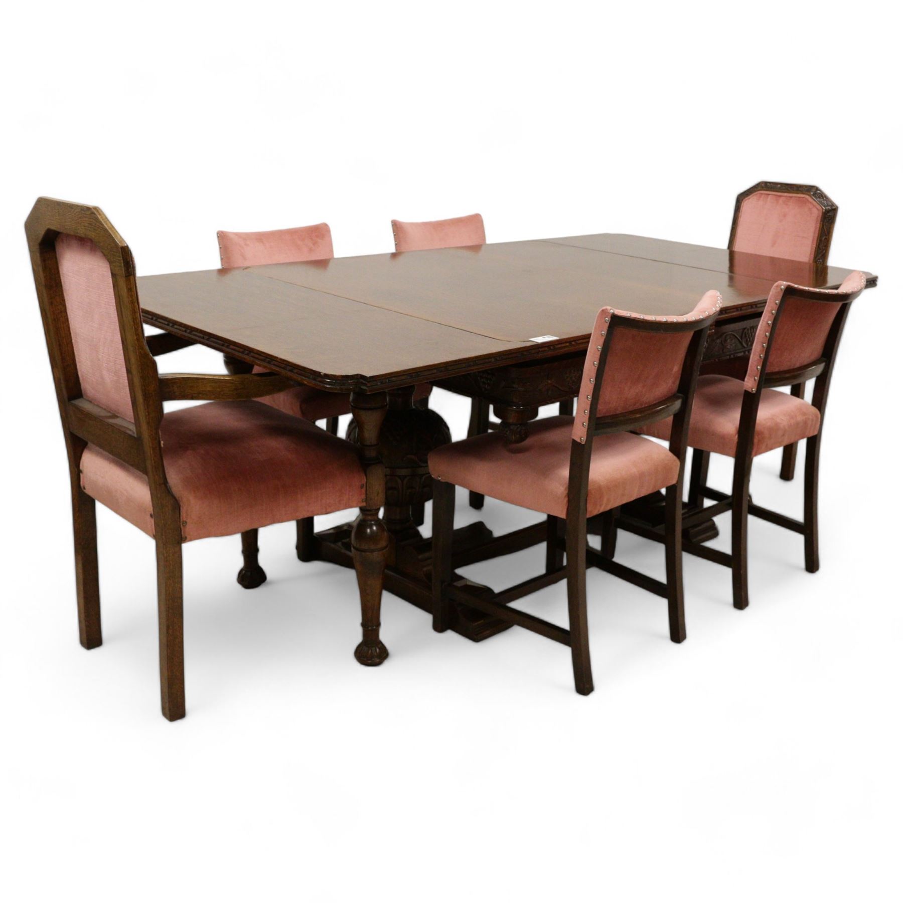 Early 20th century heavily carved oak draw leaf dining table, shaped rectangular top with recessed bead moulded edge, grape-vine carved frieze over large baluster vine and lobe carved end supports on sledge feet united by stretcher; with matched set of six dining chairs, upholstered in coral pink fabric 