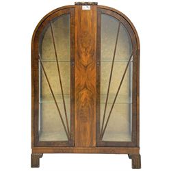 Early 20th century Art Deco walnut display cabinet, with arched top and carved floral crest, central band flanked by two glazed panel doors with decorative mullions, enclosing two glass shelves, on scroll carved bracket feet