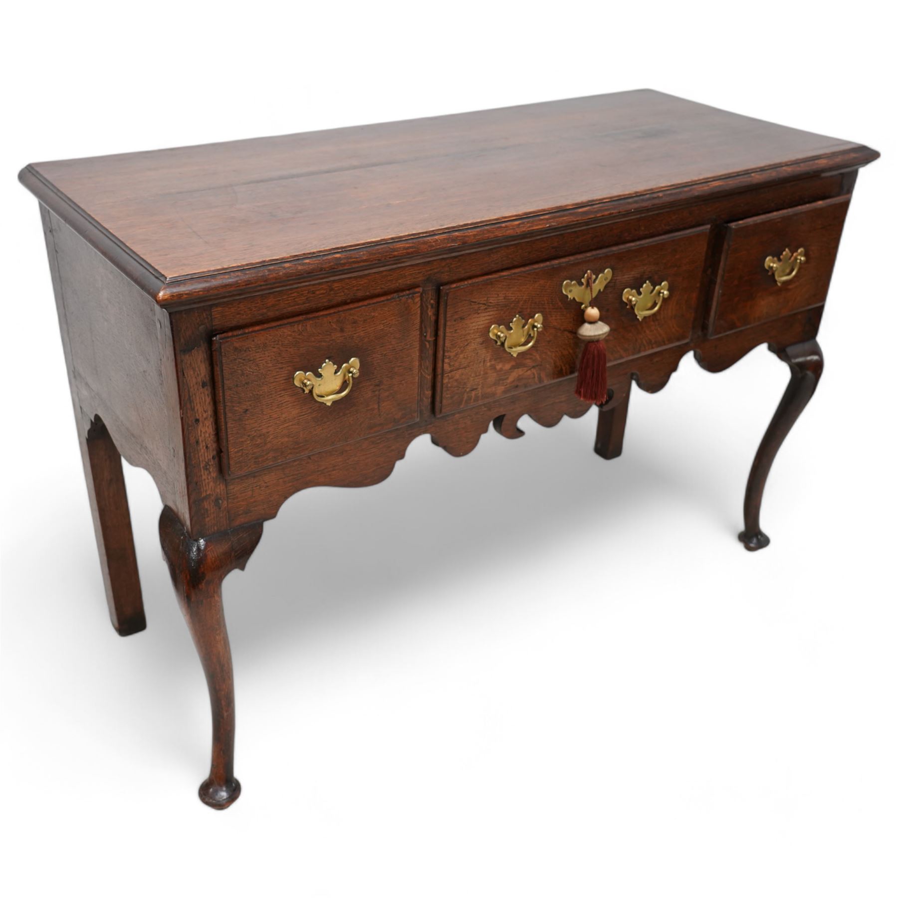 18th century oak dresser base, the rectangular top with moulded edge, fitted with three drawers with original brass handle plates, over a shaped frieze, raised on front cabriole supports with pad feet