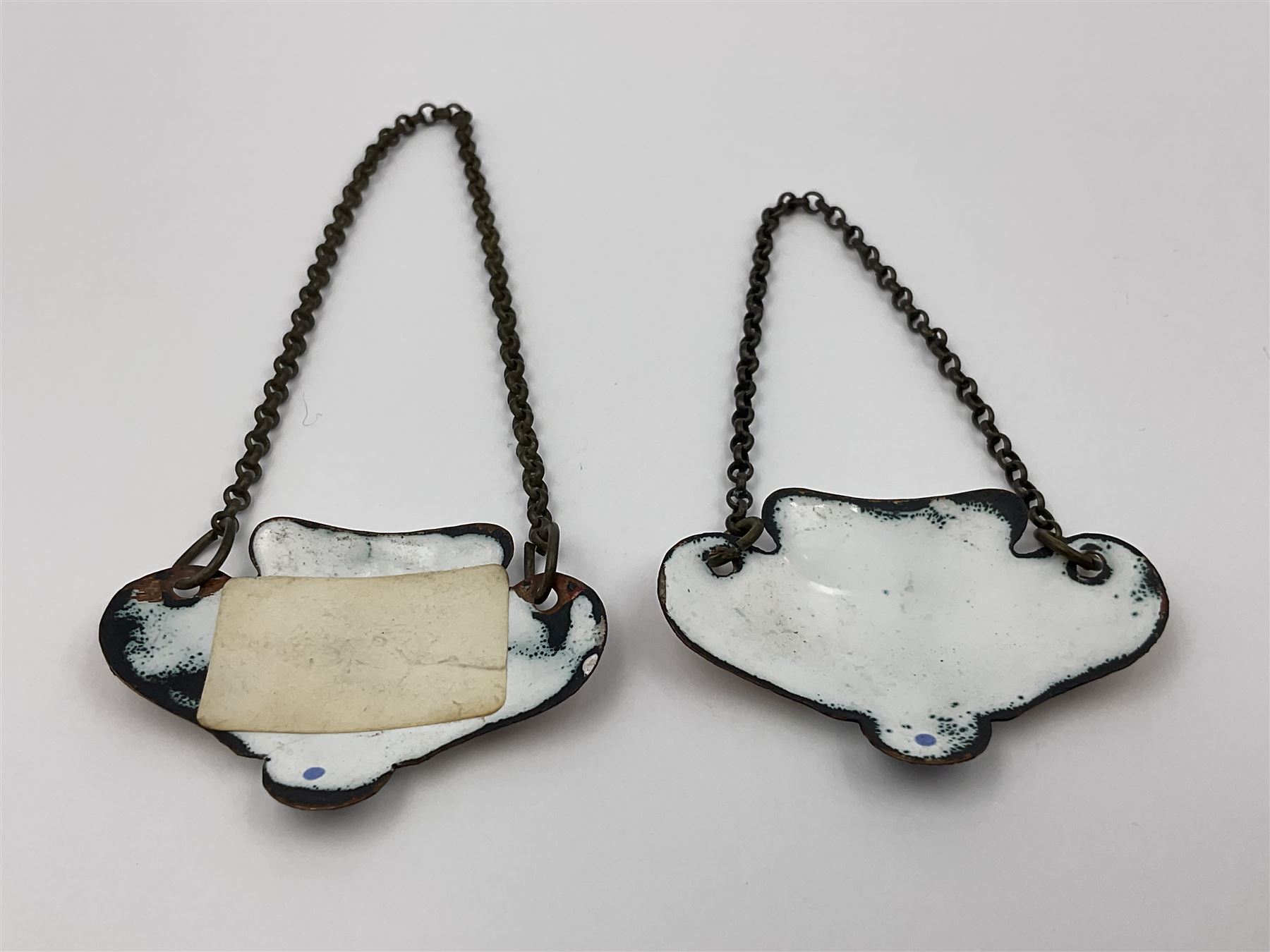 Two late 18th/early 19th century enamel wine labels, each of shaped form, titled 'CLARET', and 'SHERRY' and decorated with floral sprigs and scroll detail upon a white ground, each with suspension chain, each approximately H3.5cm W5cm