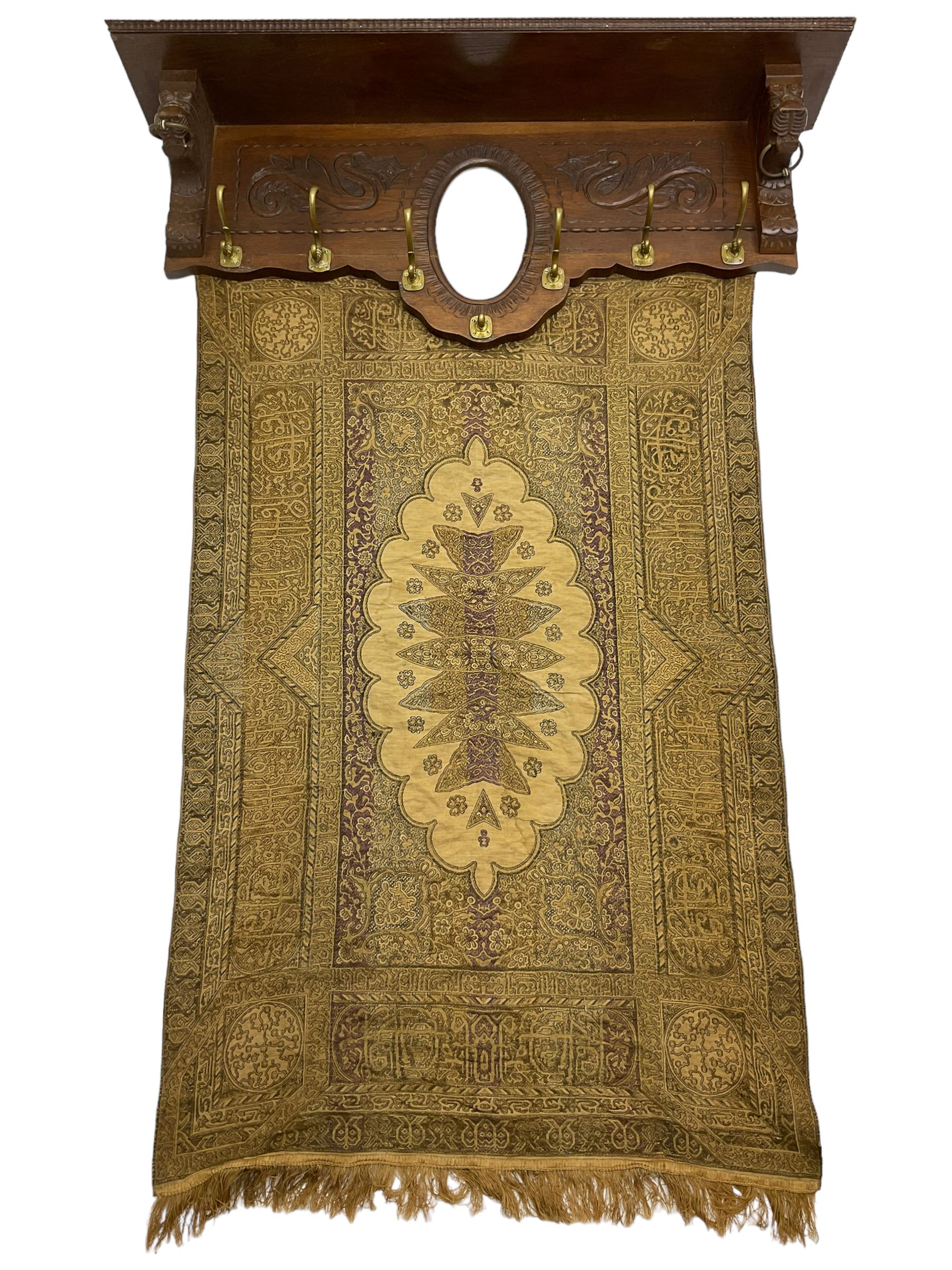 Late 20th century oak wall hanging coat rack, central bevelled oval mirror in foliate carved surround, decorated with S-scrolls and lion masks, fitted with needlework hanging 