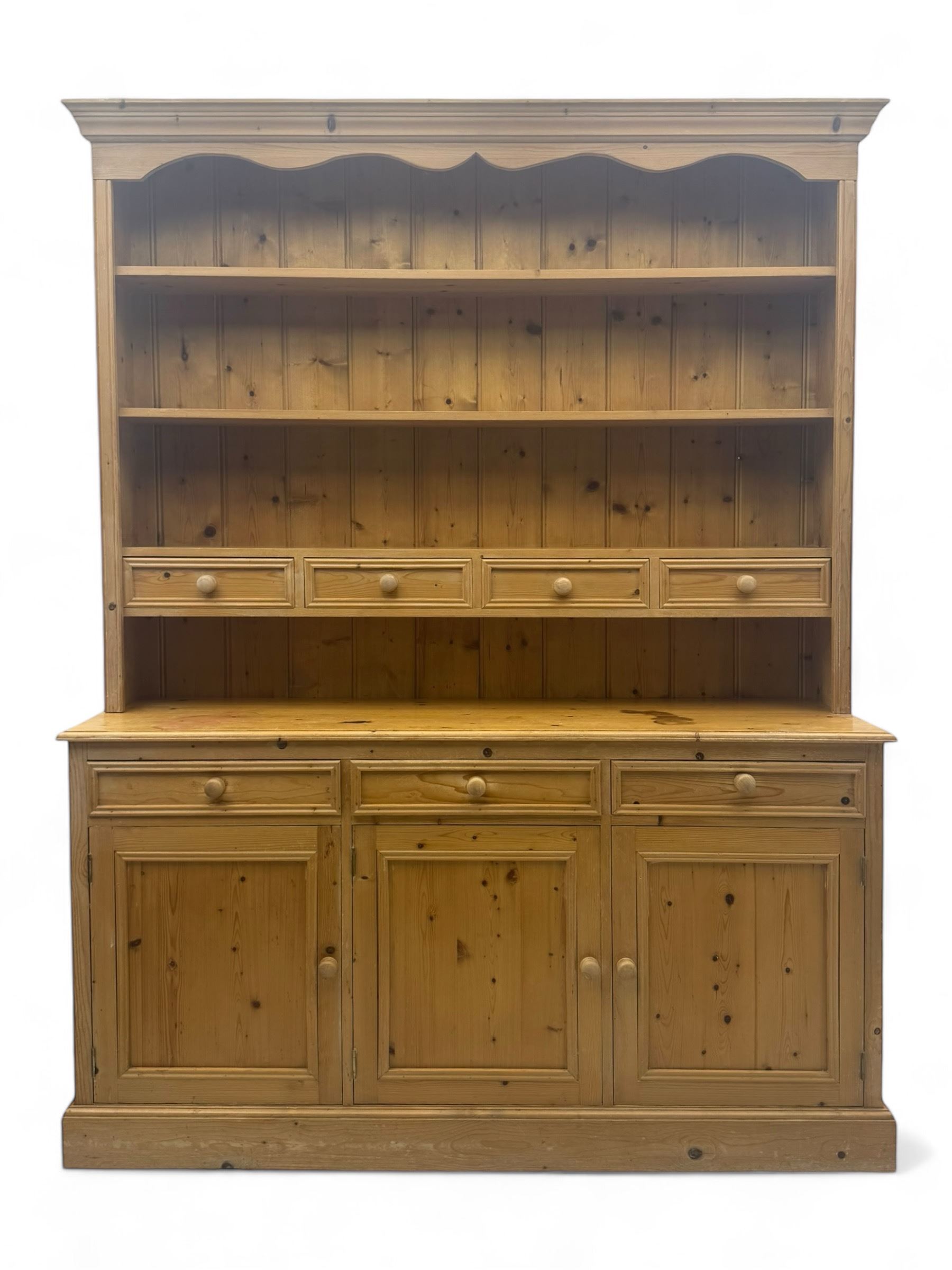 Traditional design waxed pine dresser, upper section with moulded cornice over scalloped frieze, fitted with two open shelves and four drawers, lower section with three drawers over three panelled cupboards, on plinth base