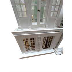 Large three storey modern dolls house, painted white with latticed windows, grey roof and metal fencing, with decorated interior, together with two dolls house garden rooms and two conservatories