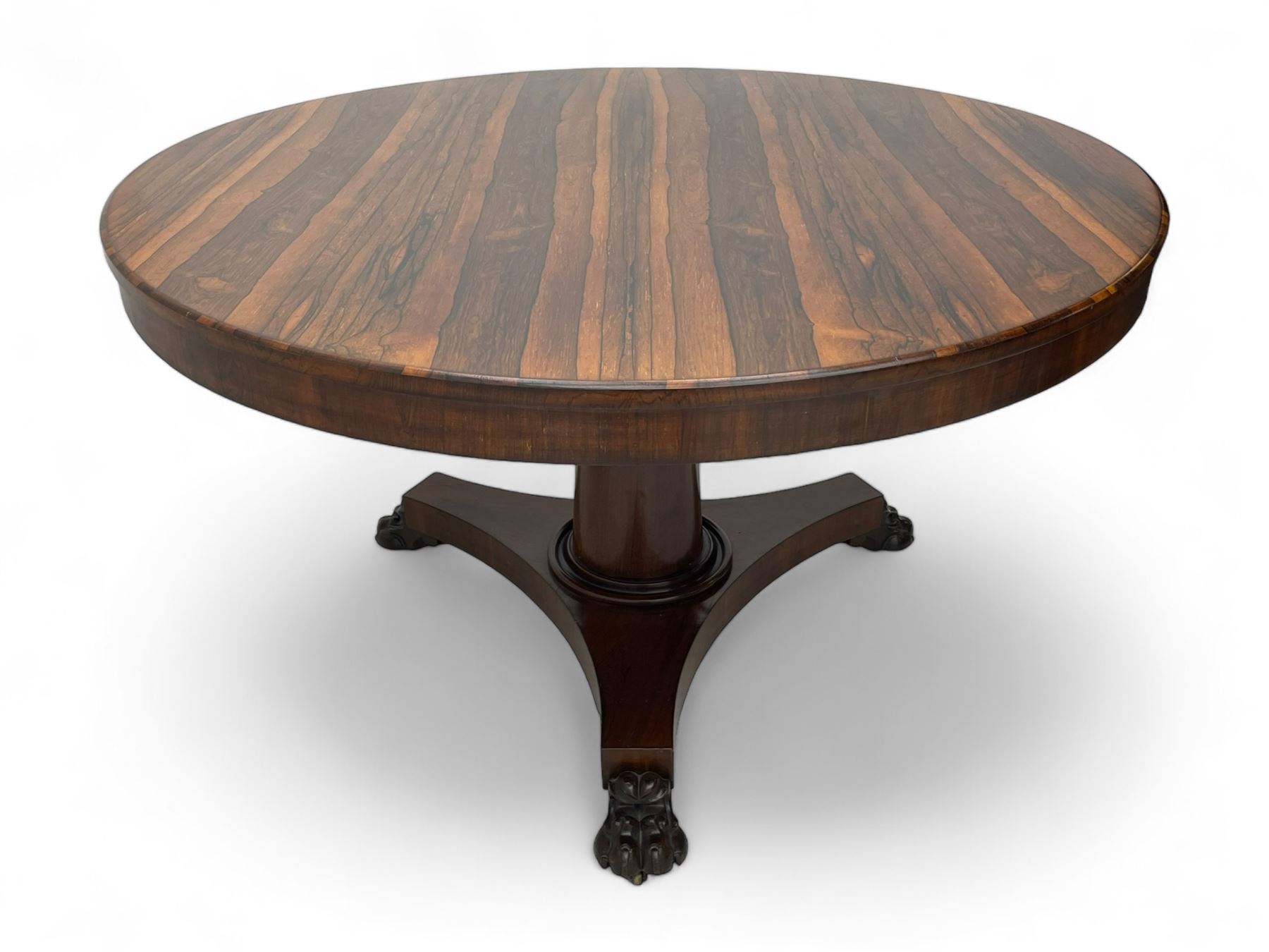 Mid-19th century rosewood breakfast or centre table, circular tilt-top on tapered barrel pedestal, concaved triangular platform, on carved paw feet with castors 