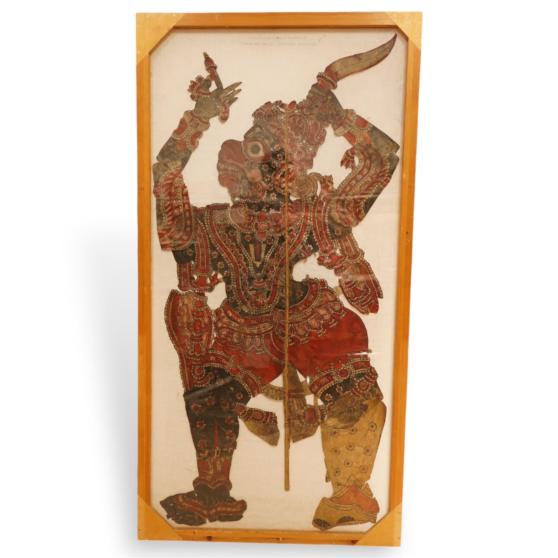 Javanese shadow puppet, painted, cut and pierced vellum, holding a knife, double sided frame 144cm x 69cm