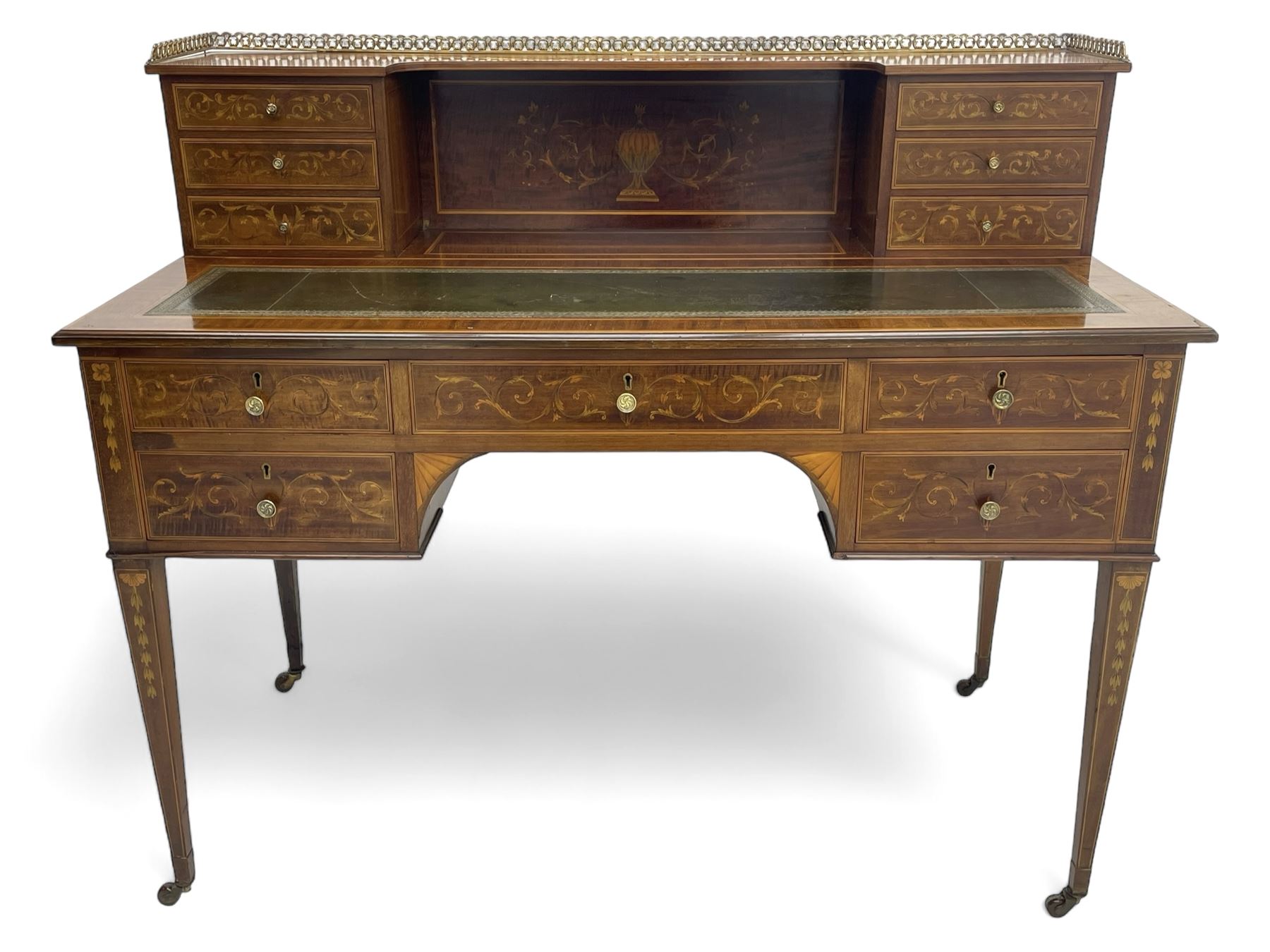 Edwardian inlaid mahogany writing desk, raised galleried back over inlaid central urn with scrolling leafy branches and six small drawers, satinwood banded rectangular moulded top with tooled leather inset, fitted with five drawers, the drawer facias inlaid with scrolling foliage and satinwood banding, square tapering supports inlaid with trailing bell flowers, on brass and ceramic castors 