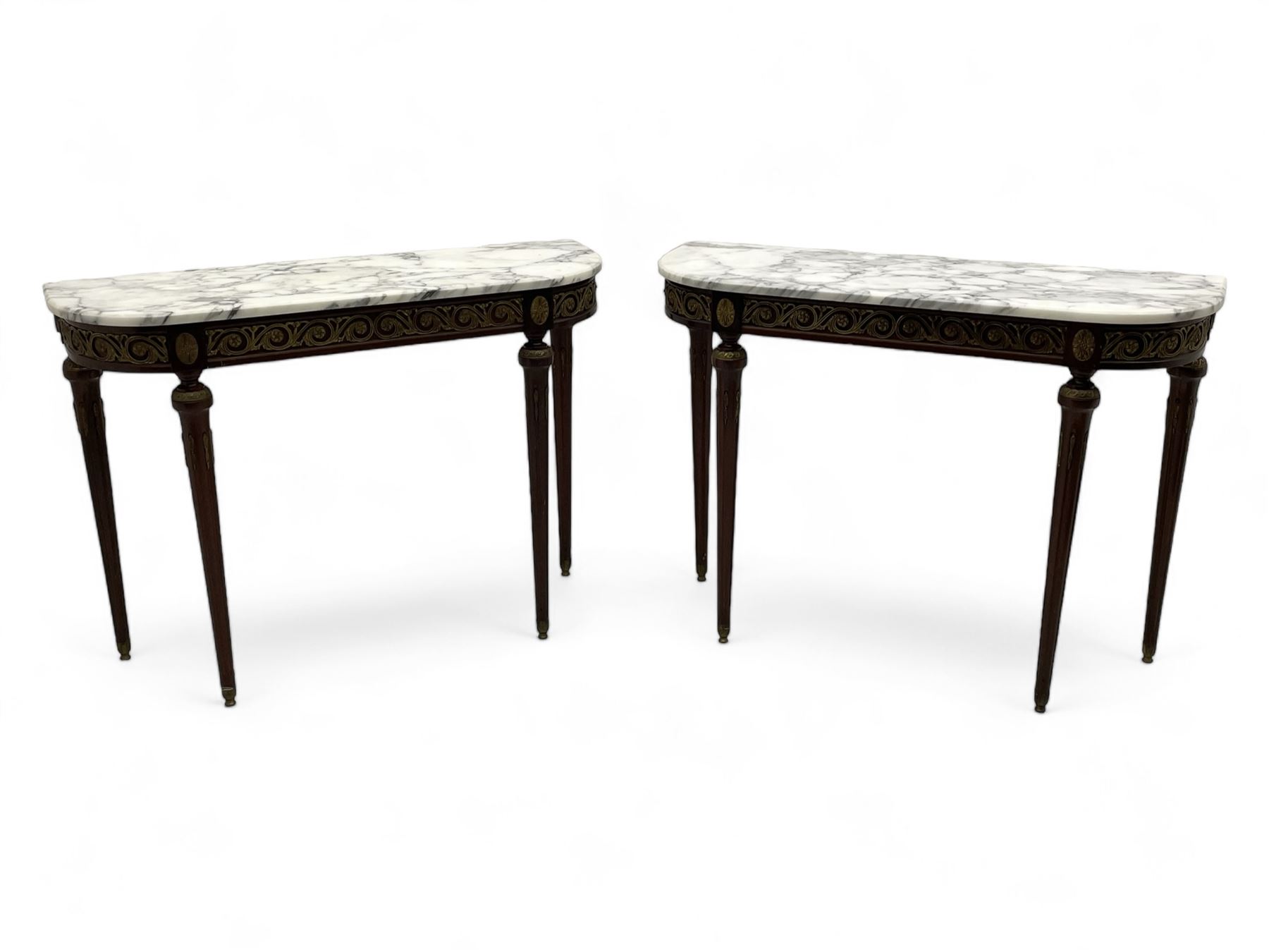 Pair of late 20th century French design mahogany console tables, D-end form with white and grey veined marble tops, the frieze rails decorated with scrolled leaf and flower head cast brass mounts, on turned and fluted supports with cast brass mounts and feet 