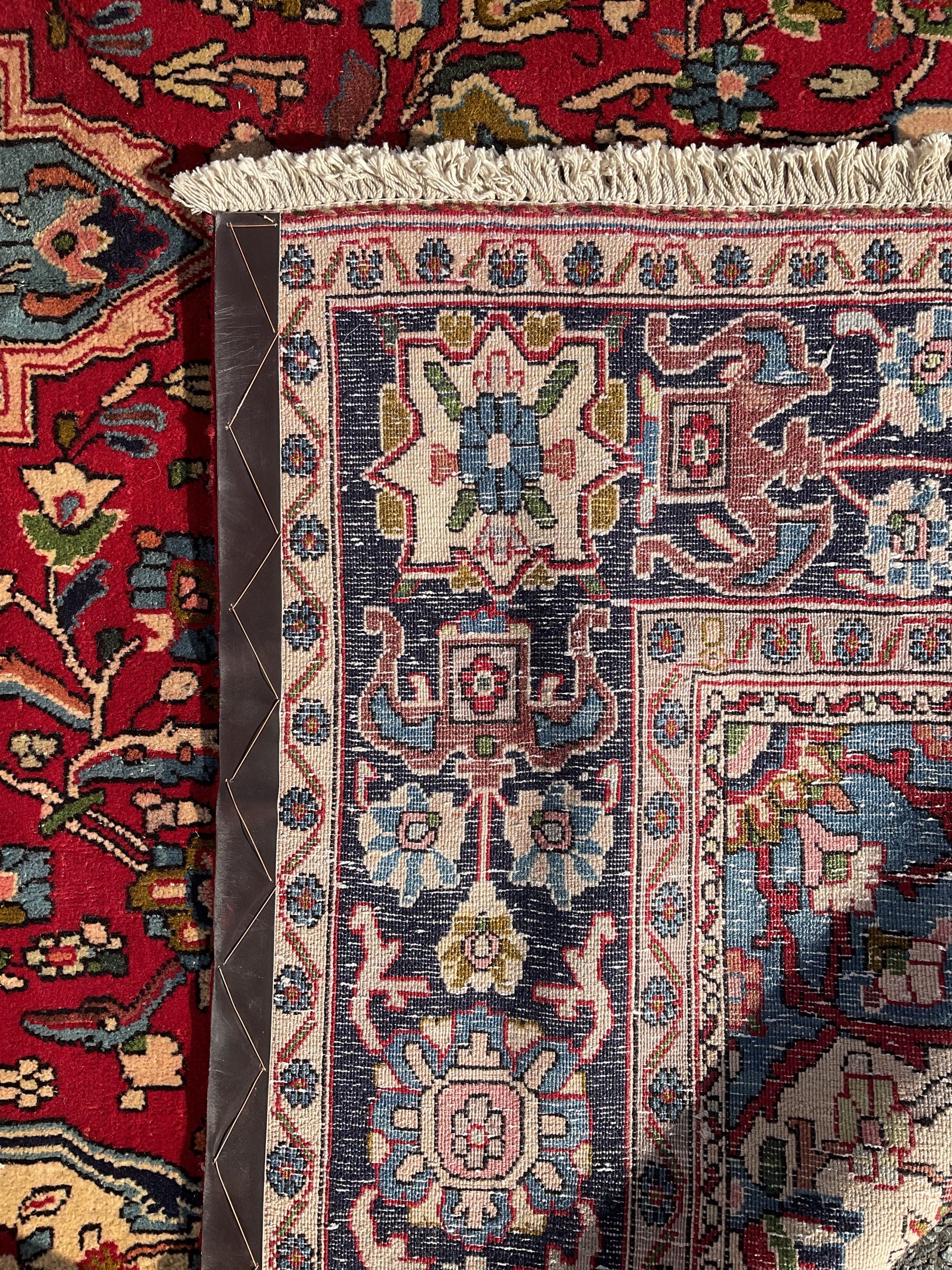 Central Persian Isfahan crimson ground carpet, central floral medallion in ivory and blue, set within a field of dense floral patterns, bordered by a navy band decorated with stylised flower heads and vines