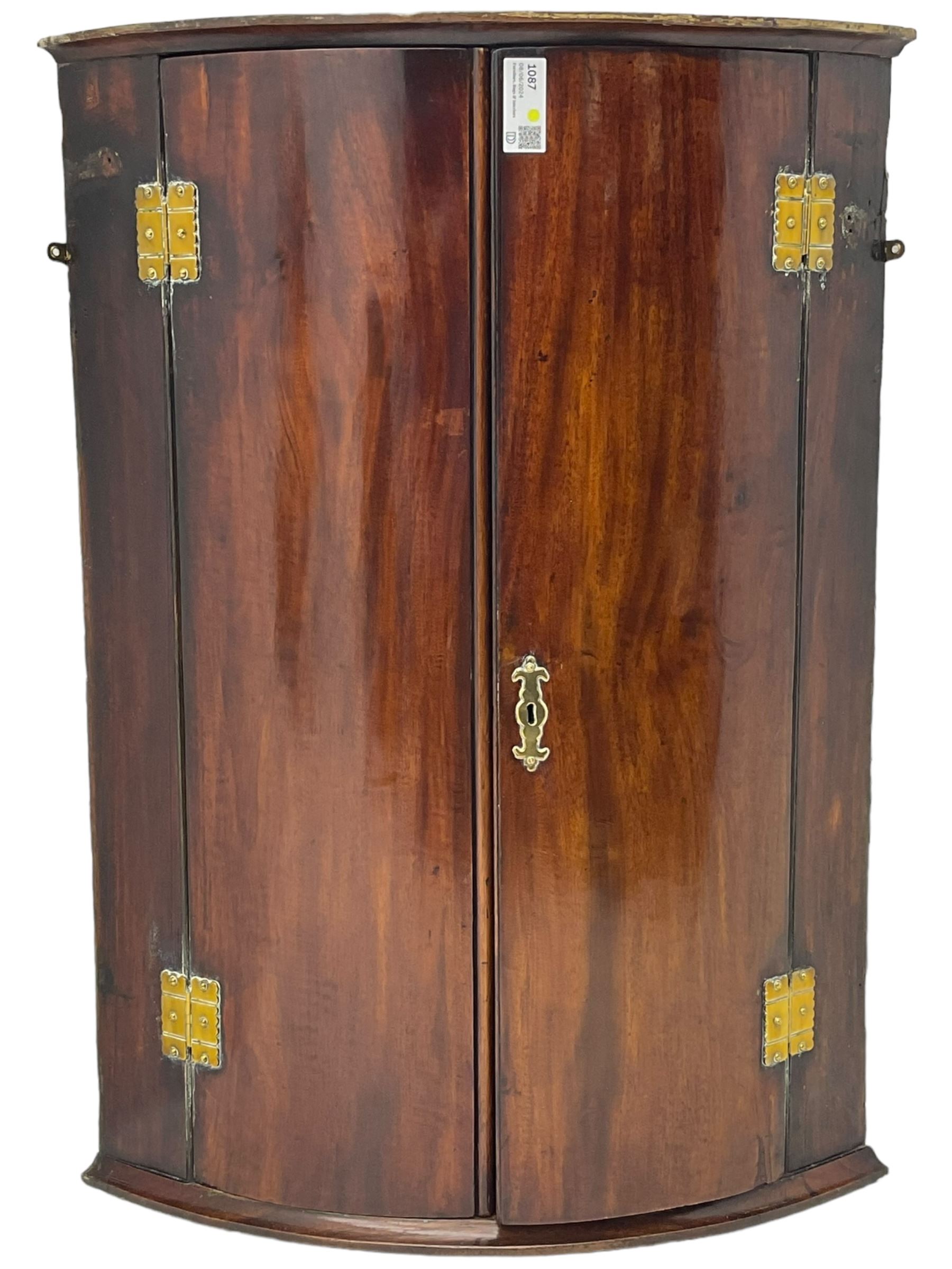 George III mahogany bow-front corner cupboard, enclosed by two figured doors with brass hinges and escutcheon, the painted interior fitted with three shelves 