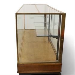 Early 20th century glazed oak and brass bound shop's display cabinet or haberdashery cabinet, fitted with two sliding glass doors, two glass shelves on chromed metal supports, black finish block feet