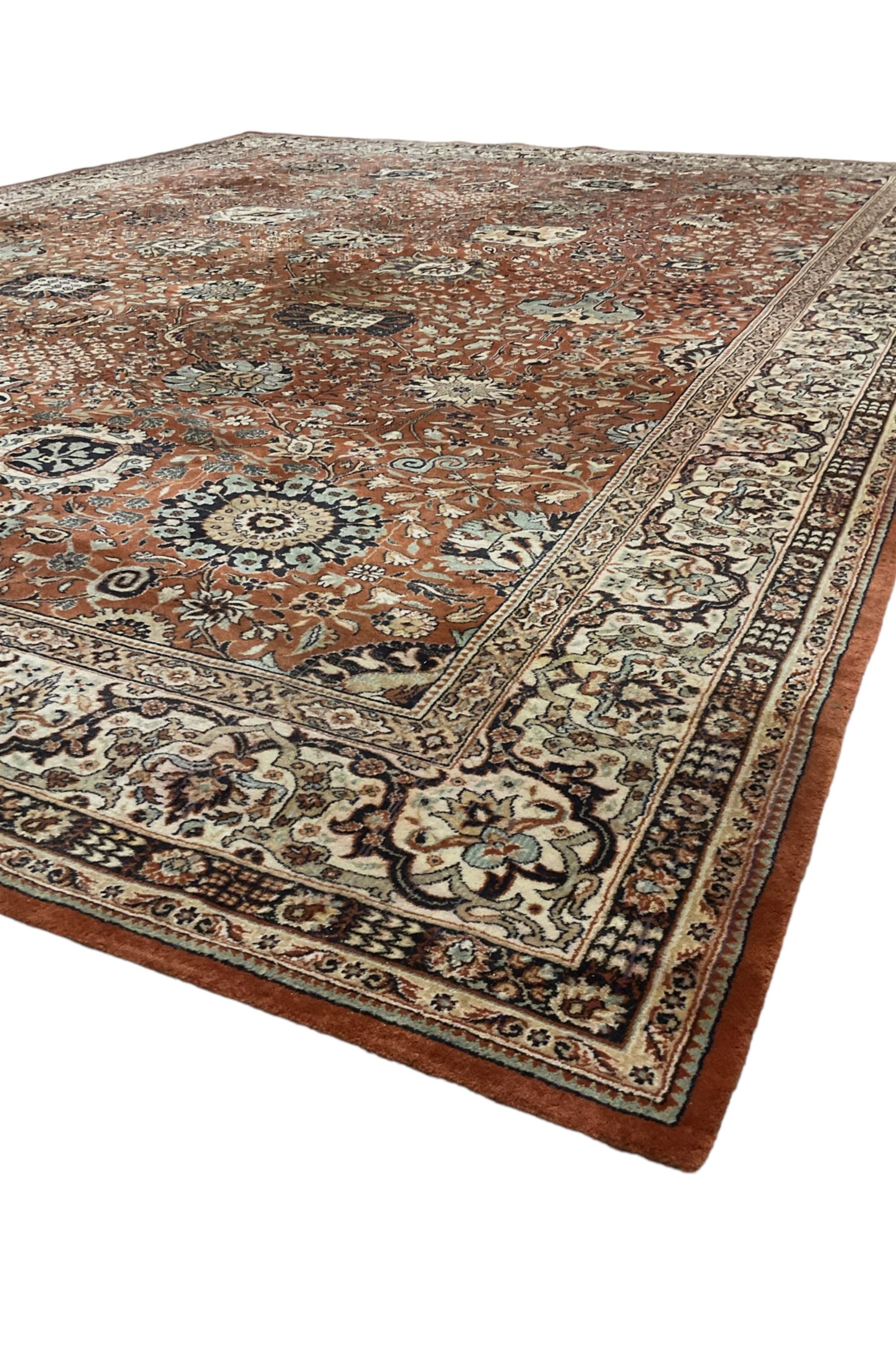 Persian design carpet, rust ground field decorated with large stylised plant motifs surrounded by smaller floral motifs, repeating trailing border