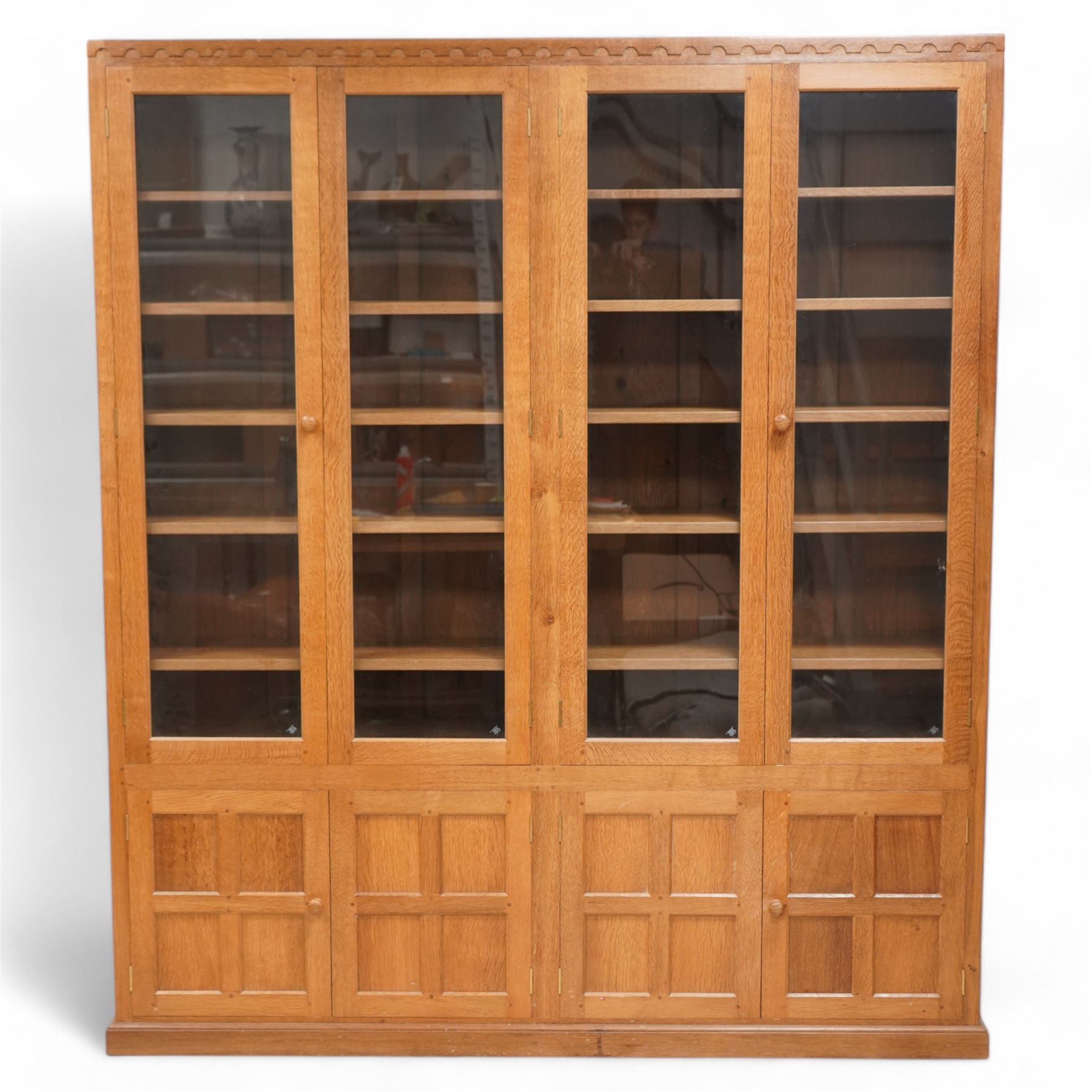 Eagleman - oak bookcase, penny moulded cresting rail over four glazed doors and four panelled doors, fitted with adjustable shelves, on moulded plinth base, panelled sides, carved with eagle signature, by Albert Jeffray, Sessay, Thirsk