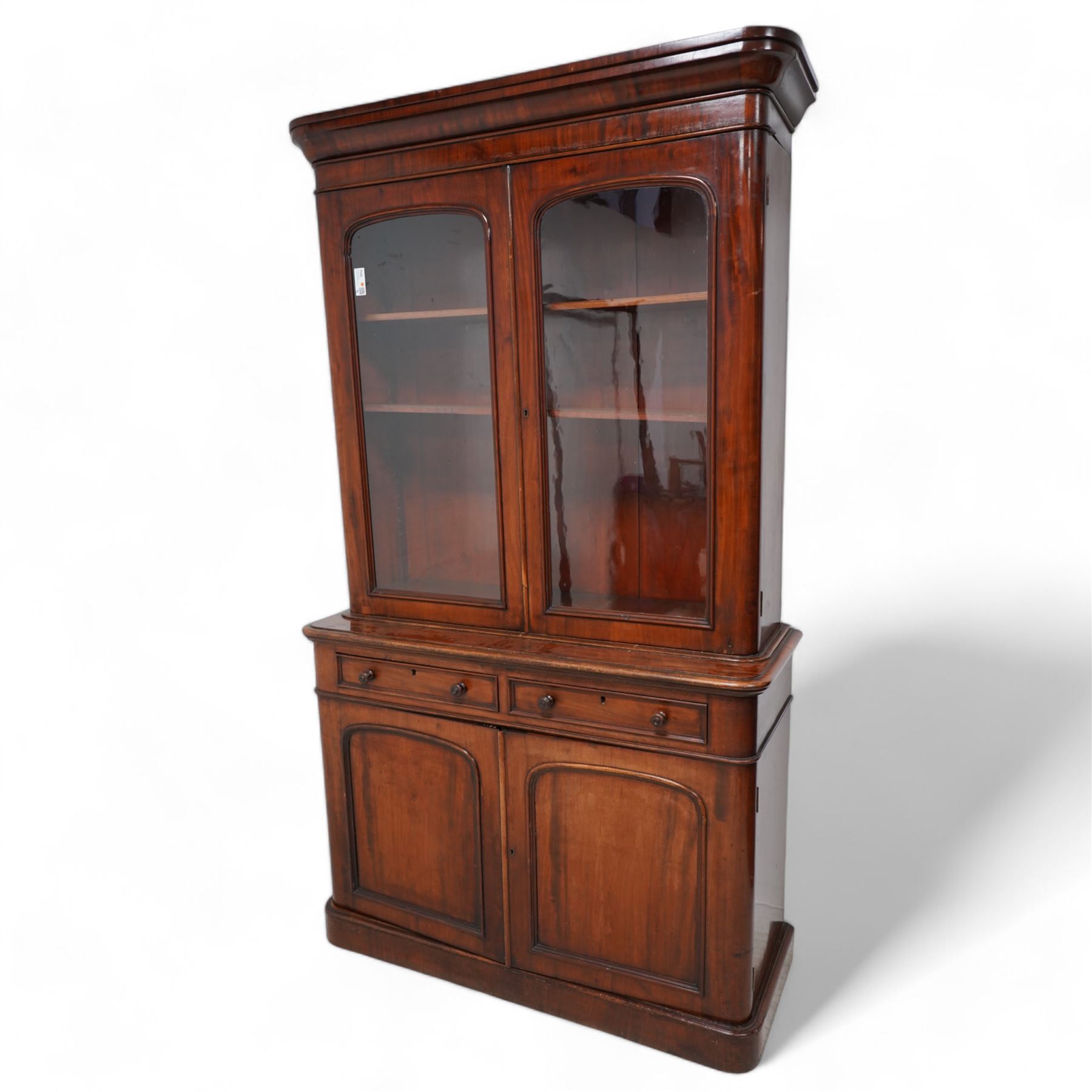 Victorian mahogany bookcase on cupboard, projecting cornice over two glazed doors, the lower section fitted with two drawers and two panelled cupboards, on moulded plinth base 