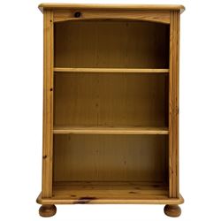 Traditional pine open bookcase, featuring arched top section flanked by fluted side supports, two adjustable shelves and cast iron coat hook with cat motif to the left side, standing on round bun feet 