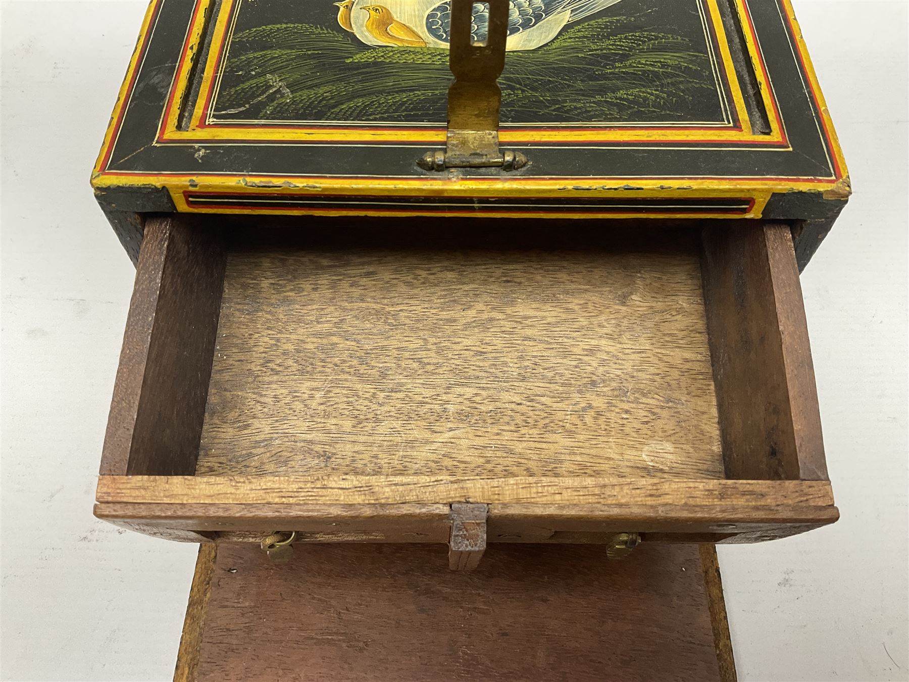 Small wooden collectors chest, painted to each side with birds upon a black ground within red and yellow borders, opening to reveal a compartmentalised interior containing one long drawer above two smaller drawers, H13cm, W18cm, D14.5cm