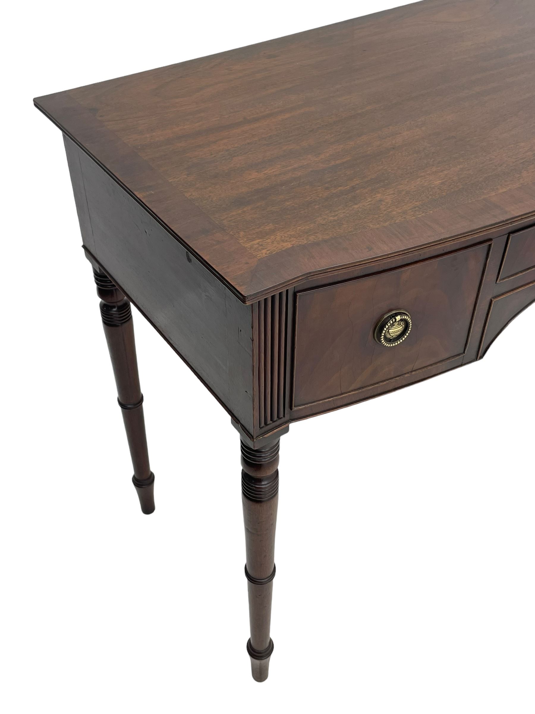 George III mahogany kneehole dressing or writing table, stepped bow-front form, reed moulded top with mahogany crossband, fitted with three cock-beaded drawers with circular pressed brass handle plates decorated with urn and beaded ring handle, on ring turned supports 