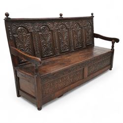 18th century oak settle or bench, moulded cresting rail with globular finials over five panel back, each stepped arch panel carved with stylised leaf decoration, hinged box seat over S-scroll foliate frieze and two panels carved with scrolling pattern, panelled sides, on stile supports terminating to turned feet 