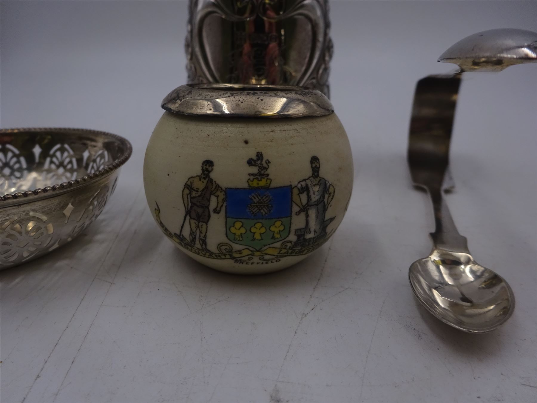 Group of silver, comprising Edwardian christening mug, of slightly tapering form, embossed with floral decoration and engraved initials and date, hallmarked Cooper Brothers & Sons Ltd, Sheffield 1906, a crested ware jar with silver collar, pierced pin dish and a pair of sugar tongs, all hallmarked 