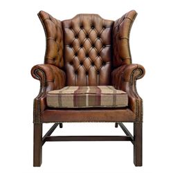 Georgian design hardwood-framed wingback armchair, shaped cresting rail and deep wingback over rolled arms, upholstered in brown buttoned leather with studwork bands, the seat cushion upholstered in checkered fabric, on square supports united by stretchers (W86cm, H118cm, D86cm); together with matching rectangular footstool (63cm x 43cm, H37cm) 