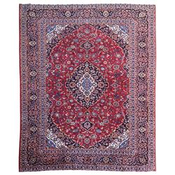 Large Kashan crimson ground carpet, central indigo medallion with stylised floral motifs, flanked by matching spandrels, bordered by multiple bands featuring repeating foliate and floral designs throughout