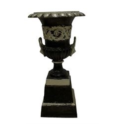 20th century cast iron Campana-shaped urn on plinth, with scrolling foliate relief decoration, in ebonised and silver painted finish