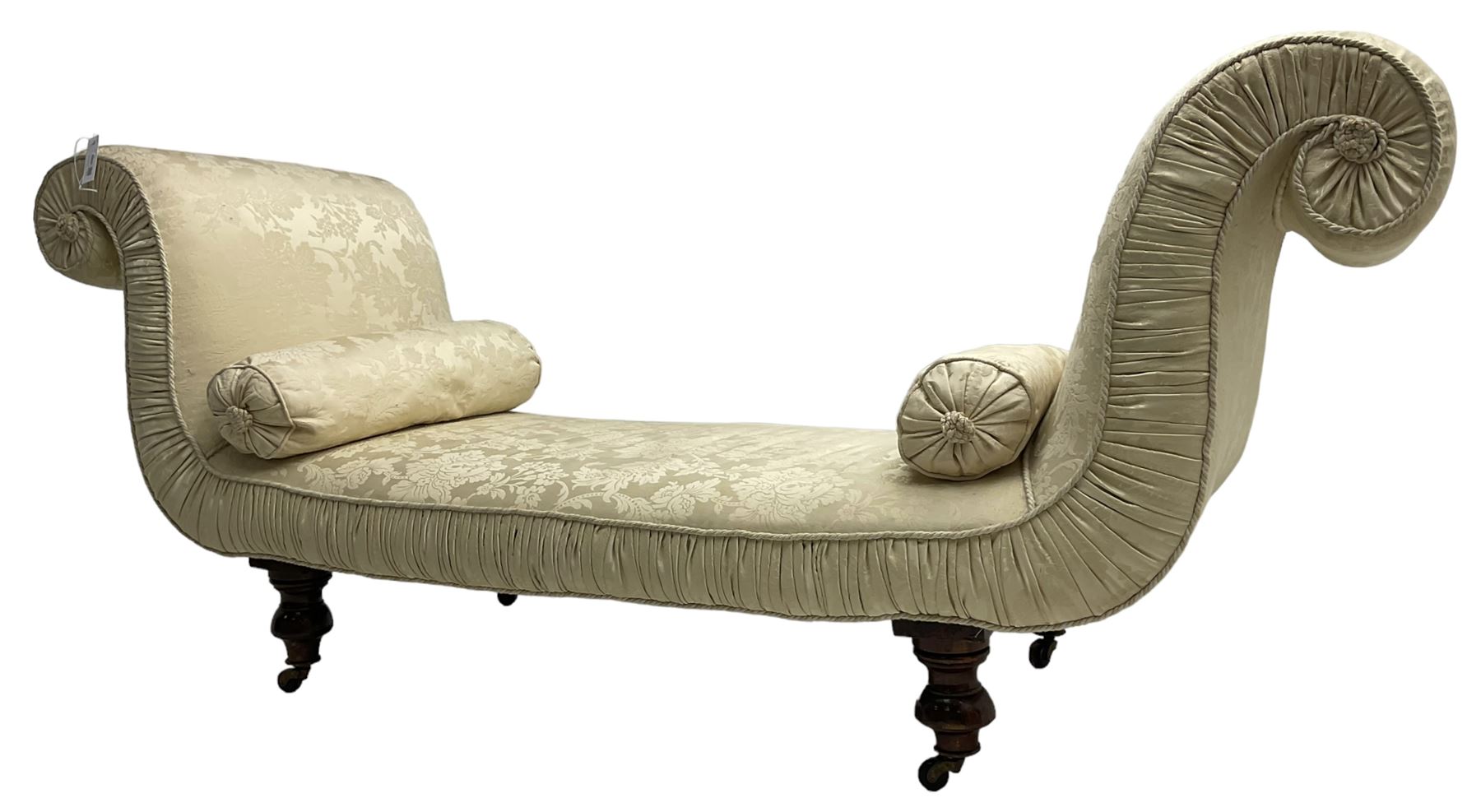 Victorian mahogany framed window seat day bed, the scrolled arms and seat upholstered in ivory foliate patterned damask fabric with matching ropetwist piping, raised on turned supports with castors