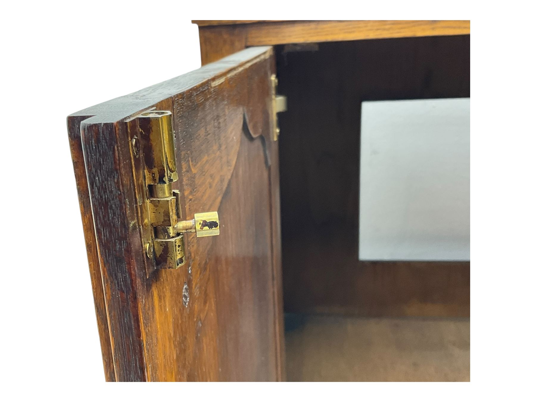 Oak drinks or media cabinet, projecting moulded cornice over two Gothic arch panelled doors on sliding tracks enclosing open storage, two drawers with brass drop handles, on bracket supports