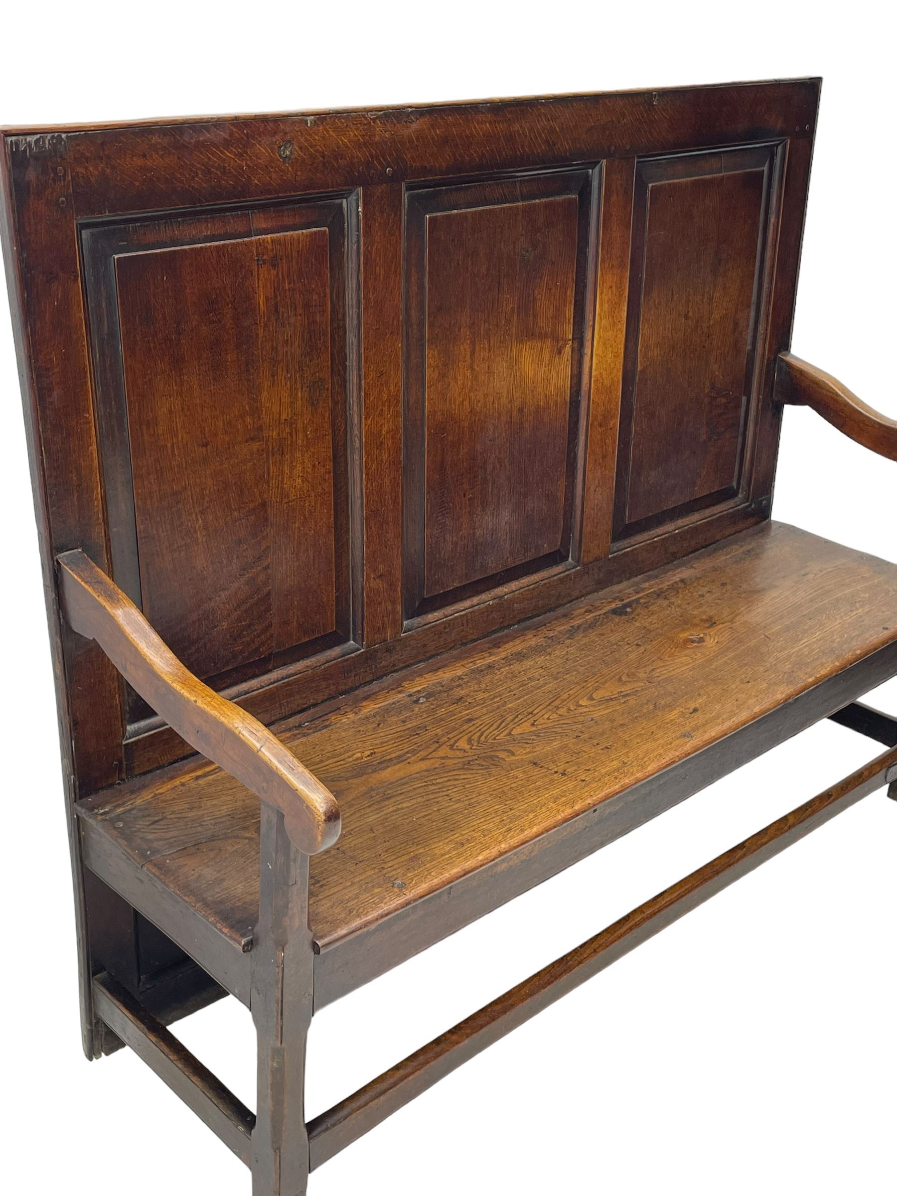 18th century oak settle, the high back with three fielded panels, shaped arms and solid plank seat, standing on square supports joined by stretchers