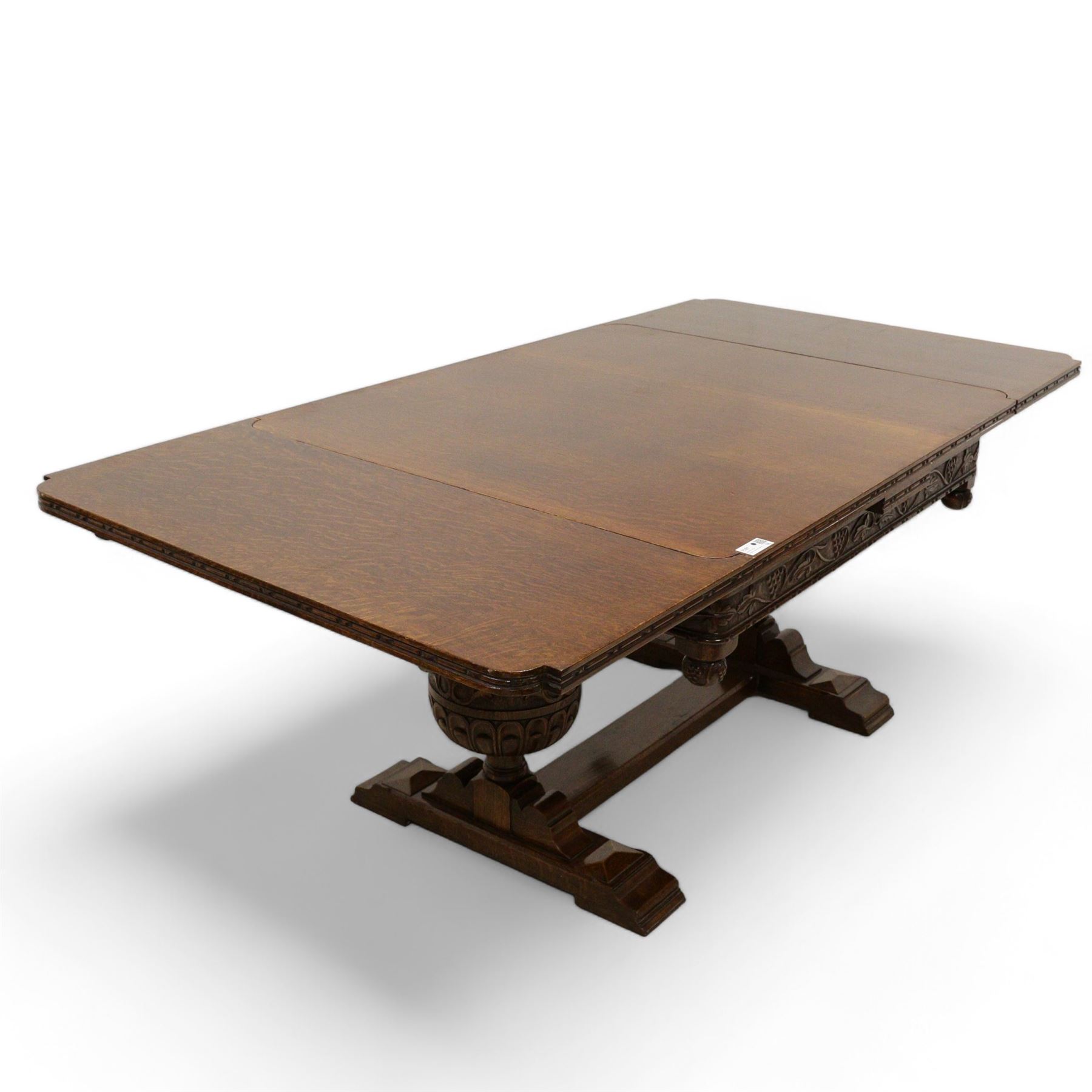 Early 20th century heavily carved oak draw leaf dining table, shaped rectangular top with recessed bead moulded edge, grape-vine carved frieze over large baluster vine and lobe carved end supports on sledge feet united by stretcher; with matched set of six dining chairs, upholstered in coral pink fabric 