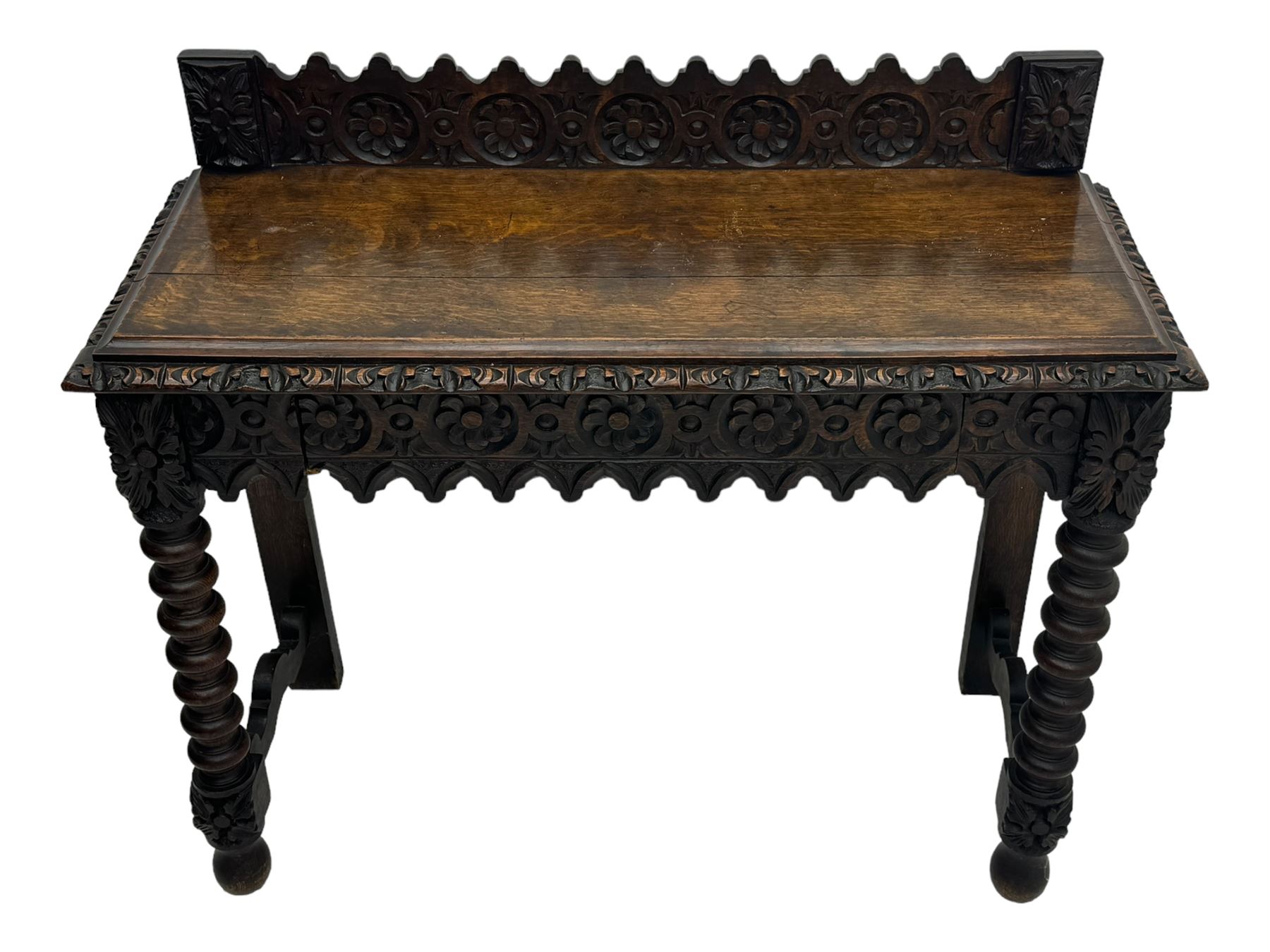 Victorian Gothic revival style carved oak console table, rectangular top with carved edge and raised back gallery, over deeply carved apron with floral and foliate motifs and central drawer, barley twist front supports and plain rear supports united by shaped stretchers, on front bun feet