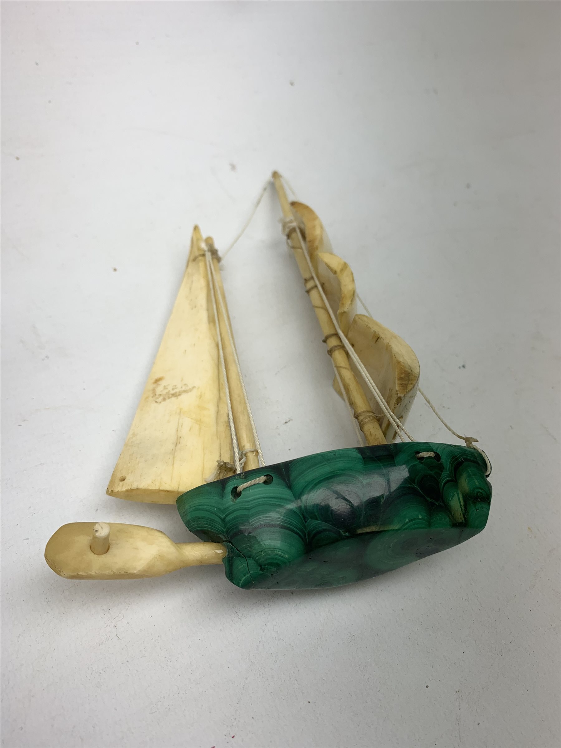 A Japanese carved ivory model of a sailing boat, surmounted by three carved figures (a/f), L22.5cm, together with a smaller sail boat with malachite hull and ivory sails and rudder, H18cm. 