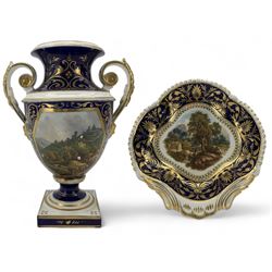 Early 19th century Derby porcelain urn, the reserve painted with a pastoral landscape and castle in the distance, with twin scroll and mask handles, upon a square pedestal base, H23cm, together with a Derby shell-shaped dish, centrally hand painted with a landscape scene titled 'In North Wales', within a cobalt blue and gilt border, L25cm (2)