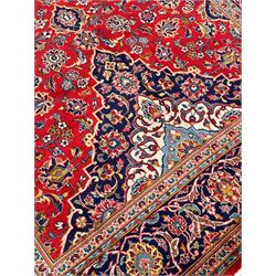 Persian Kashan crimson ground rug, overall arabesque design, the field decorated with swirled leafy branches and palmettes, indigo ground border decorated with repeating pattern, within guard stripes 