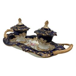 19th century porcelain inkstand, the oblong twin handled base centrally painted with a floral bouquet, flanked by two footed inkwells and covers, with rococo-inspired acanthus moulded borders and handles, pattern no. 2/3339, L26.5cm 