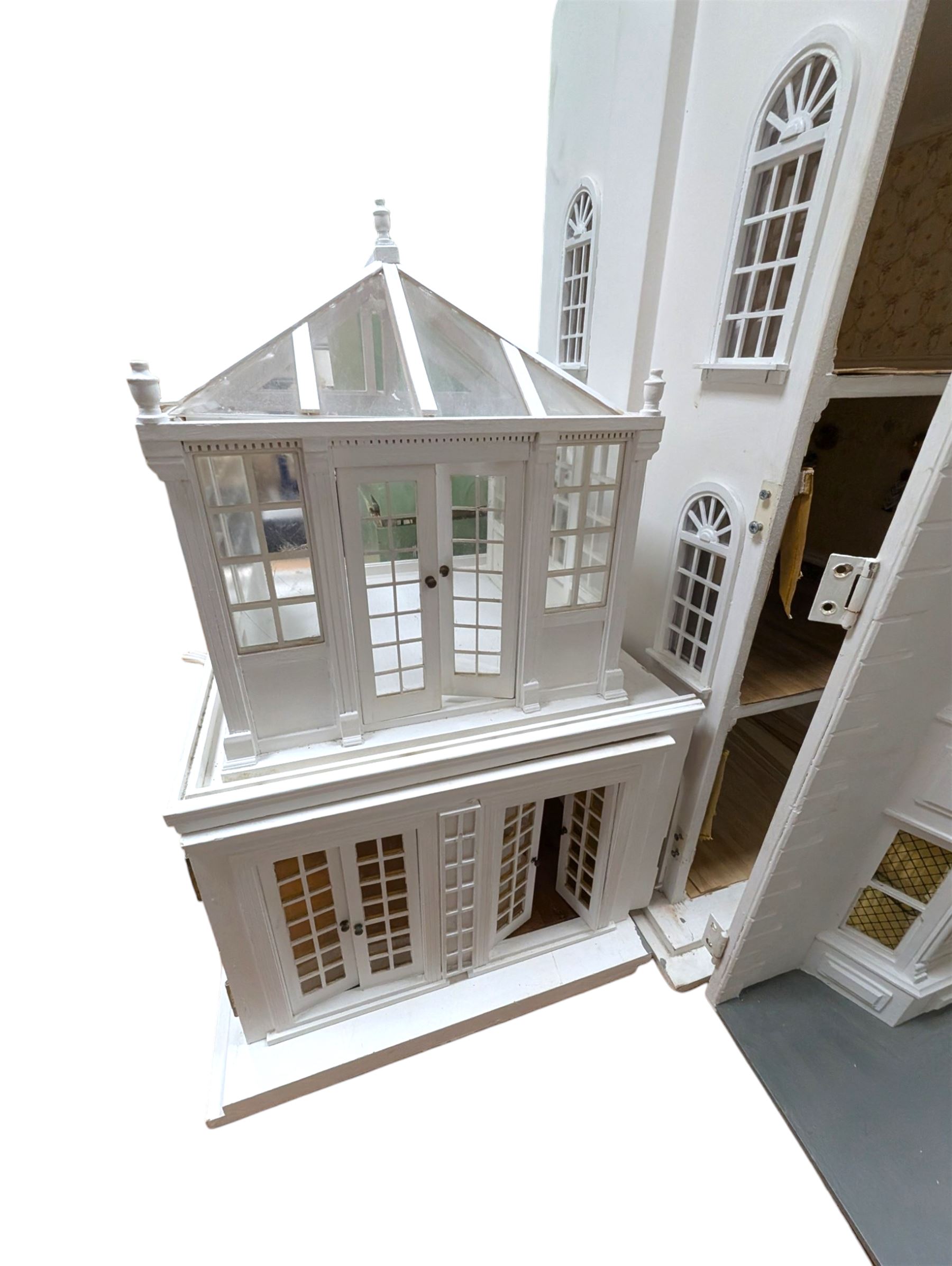 Large three storey modern dolls house, painted white with latticed windows, grey roof and metal fencing, with decorated interior, together with two dolls house garden rooms and two conservatories