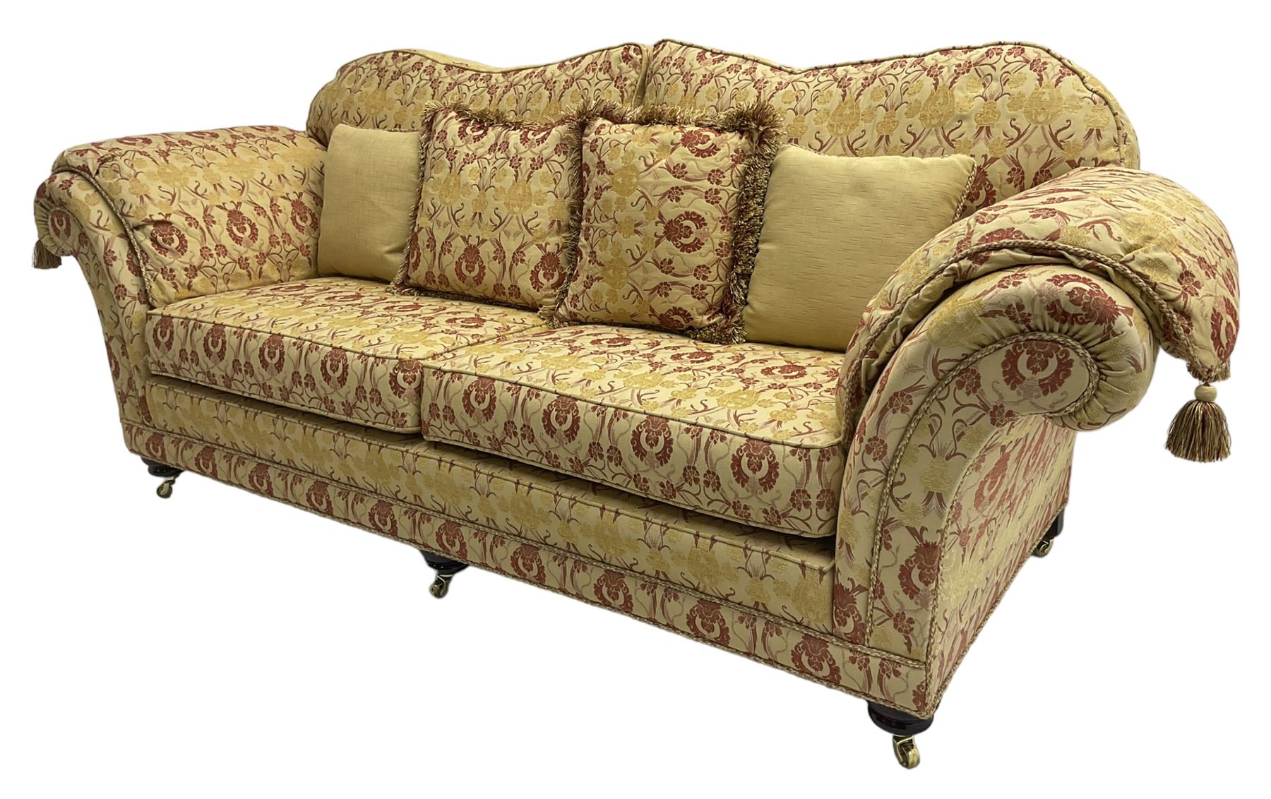 Steed Upholstery Ltd. - 'Lincoln' three-seat sofa upholstered in gold 'Olympia' floral pattern corded and tasselled fabric, together with scatter cushions and arm covers, on turned feet with brass castors