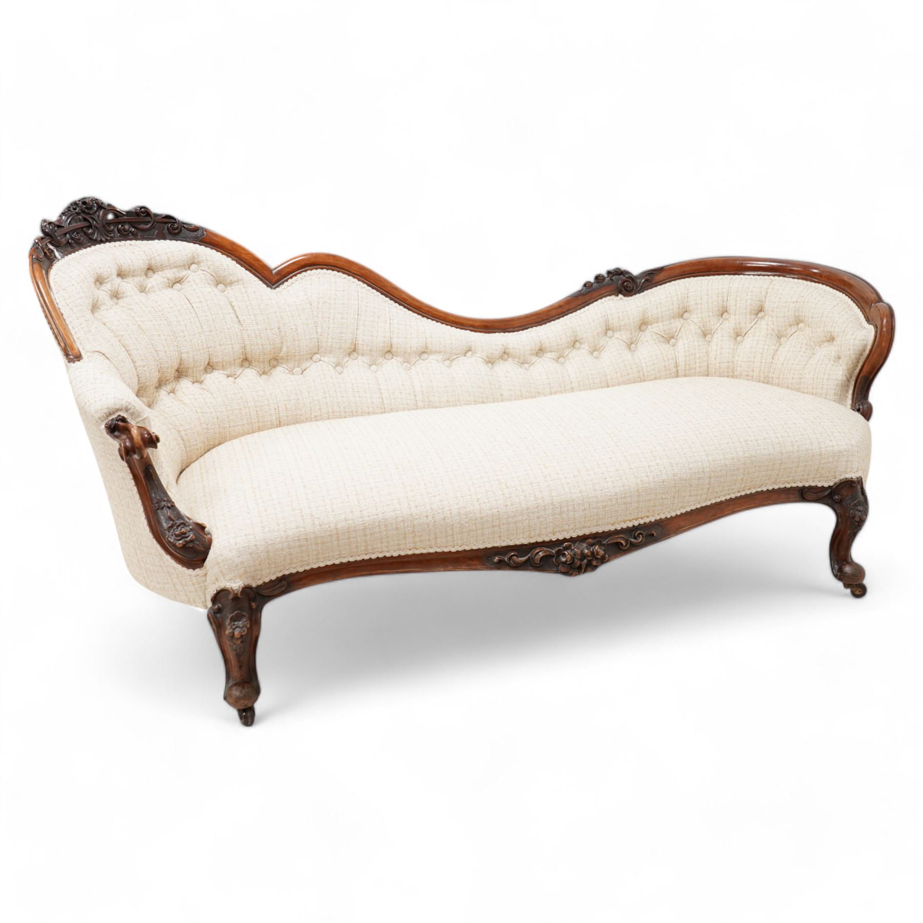 Victorian walnut framed chaise longue, the shaped frame carved with scrolls and flower heads, upholstered in buttoned textured cream fabric, the shaped seat rail carved with flower heads and extending foliate scrolls, on floral carved cabriole feet with castors 