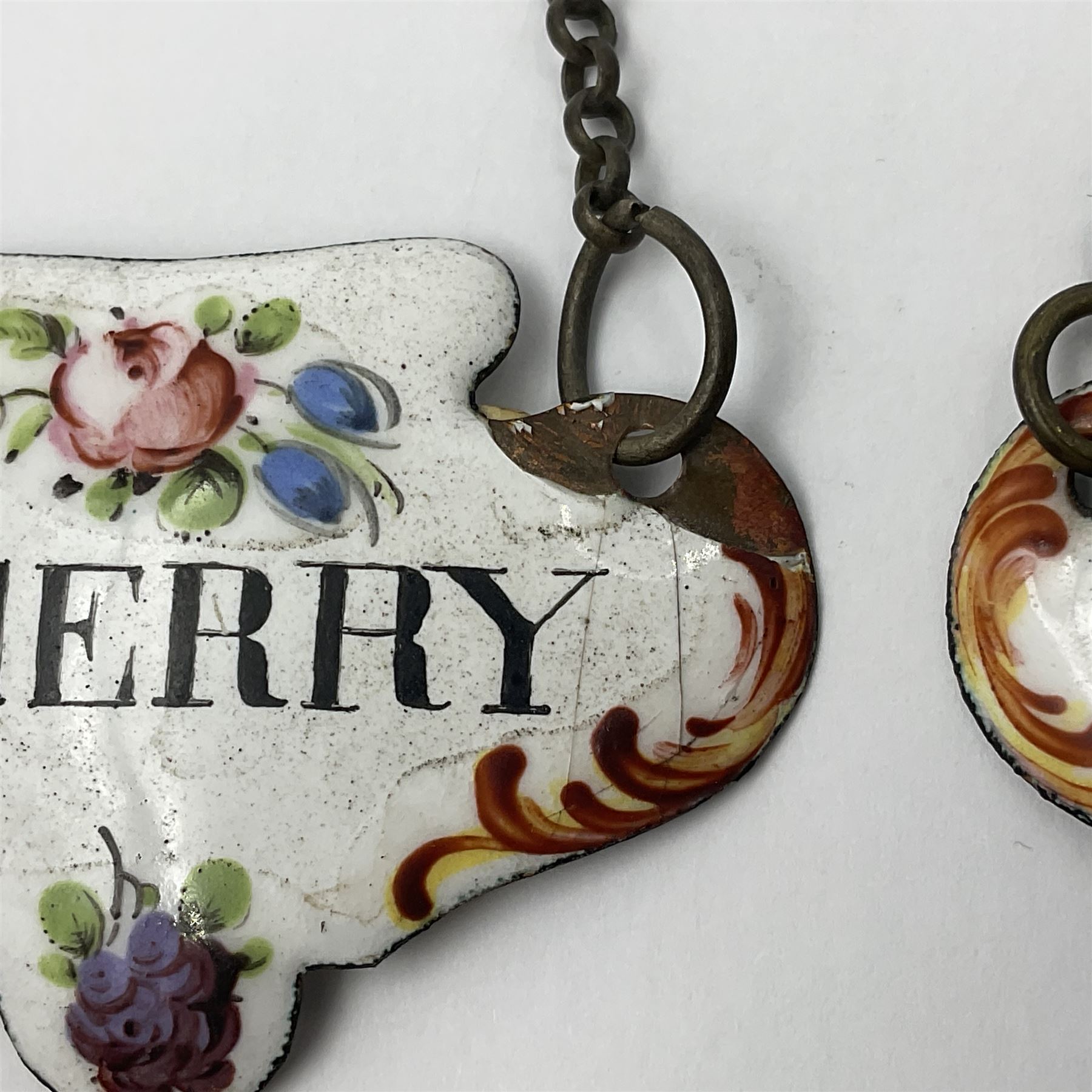 Two late 18th/early 19th century enamel wine labels, each of shaped form, titled 'CLARET', and 'SHERRY' and decorated with floral sprigs and scroll detail upon a white ground, each with suspension chain, each approximately H3.5cm W5cm