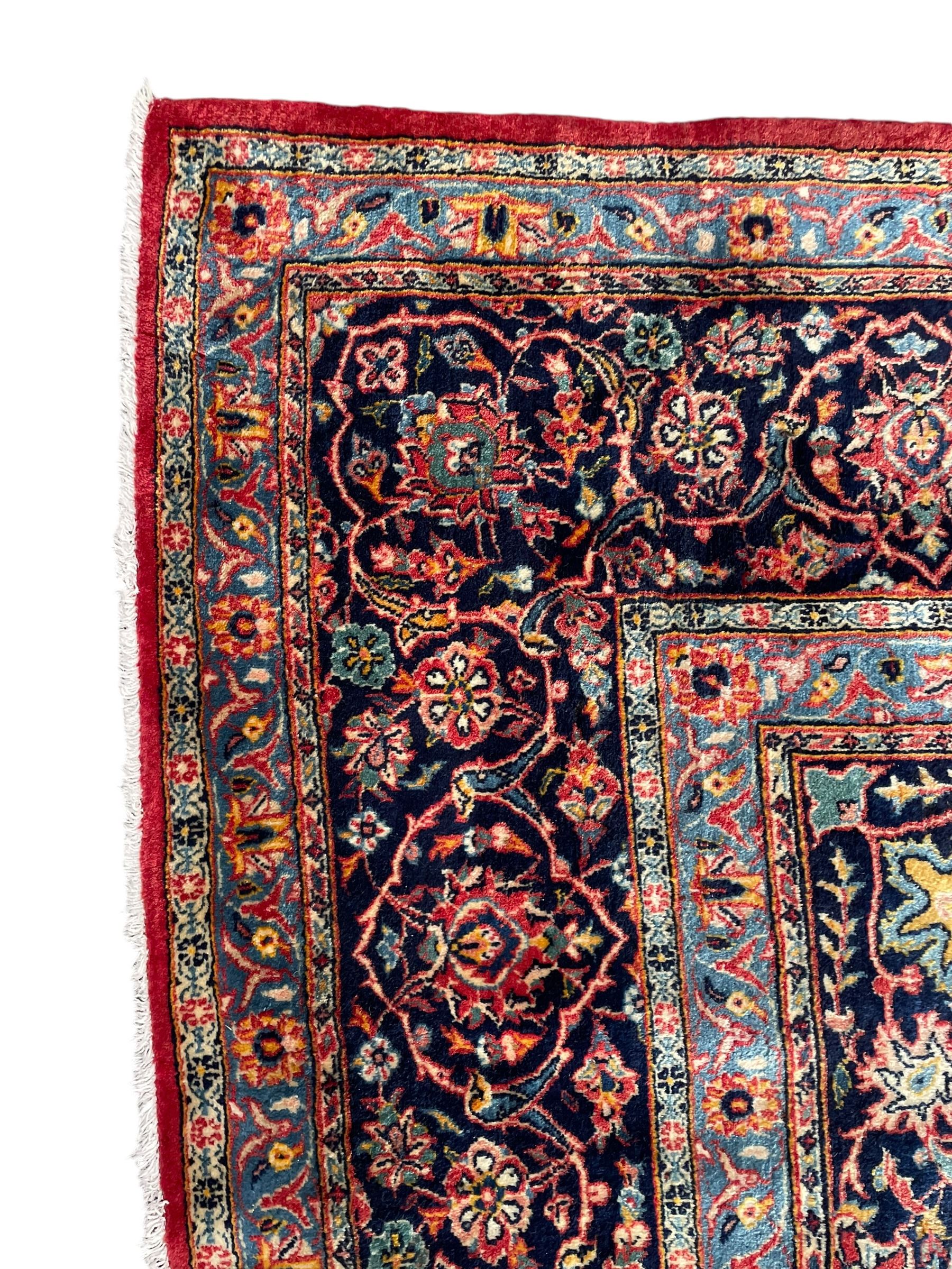 Persian Kashan crimson ground carpet, central rosette medallion on a field of trailing foliate branches decorated with palmettes, scrolling border with repeating plant motifs and flower heads, enclosed within floral pattern guard stripes