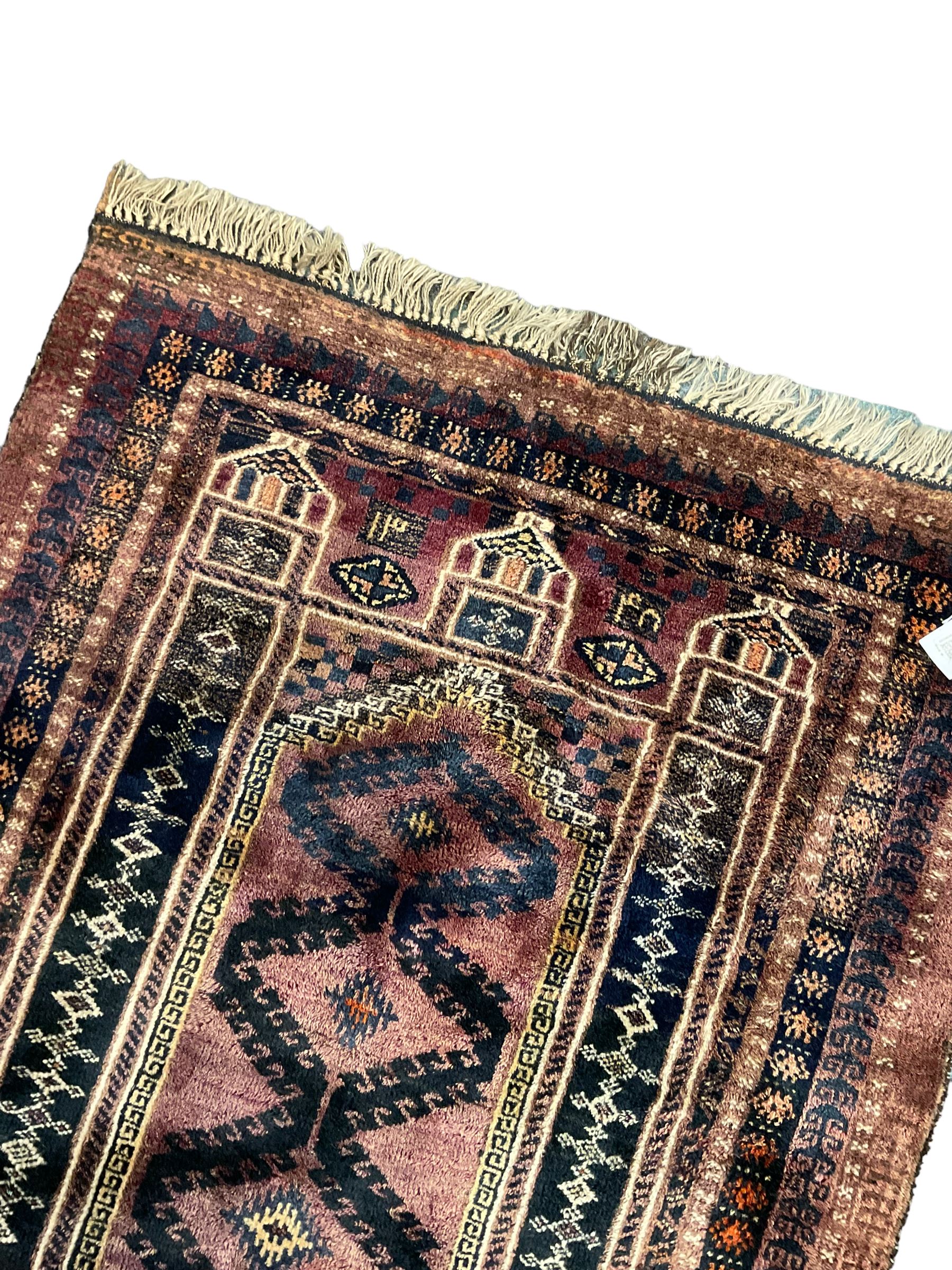 Persian prayer purple ground, decorated with three pointed buildings over tailing lozenge patterned field (111cm x 82cm); and a small Persian rug or mat, overall geometric design (81cm x 56cm)